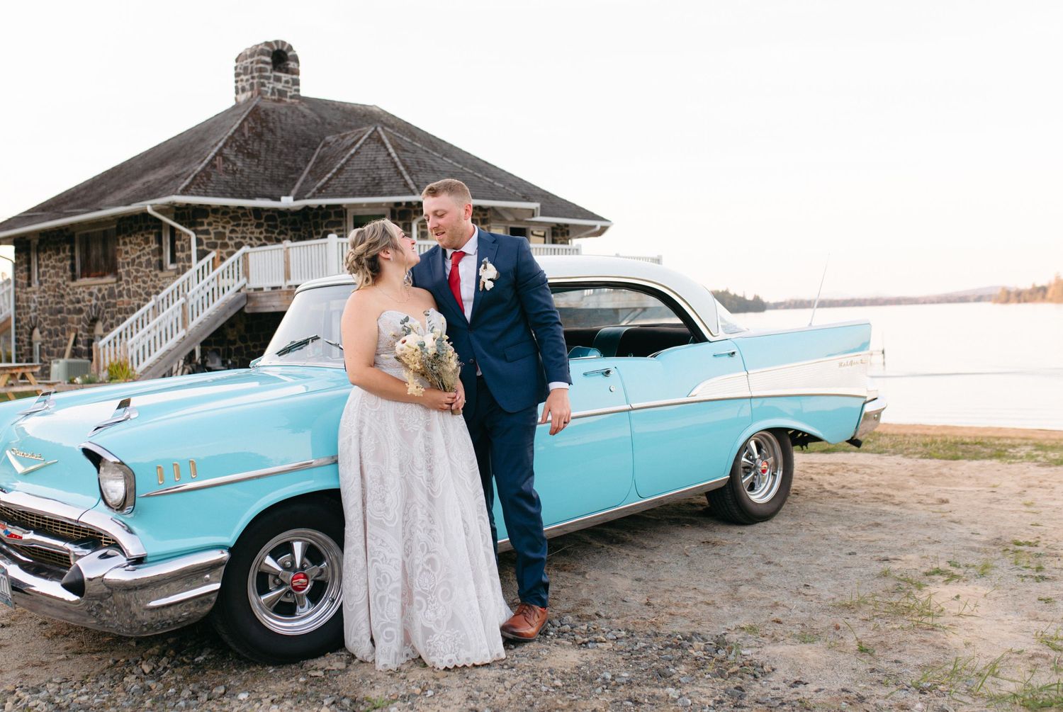 A classic light blue vintage car serves as backdrop for wedding photos by a rustic barn.