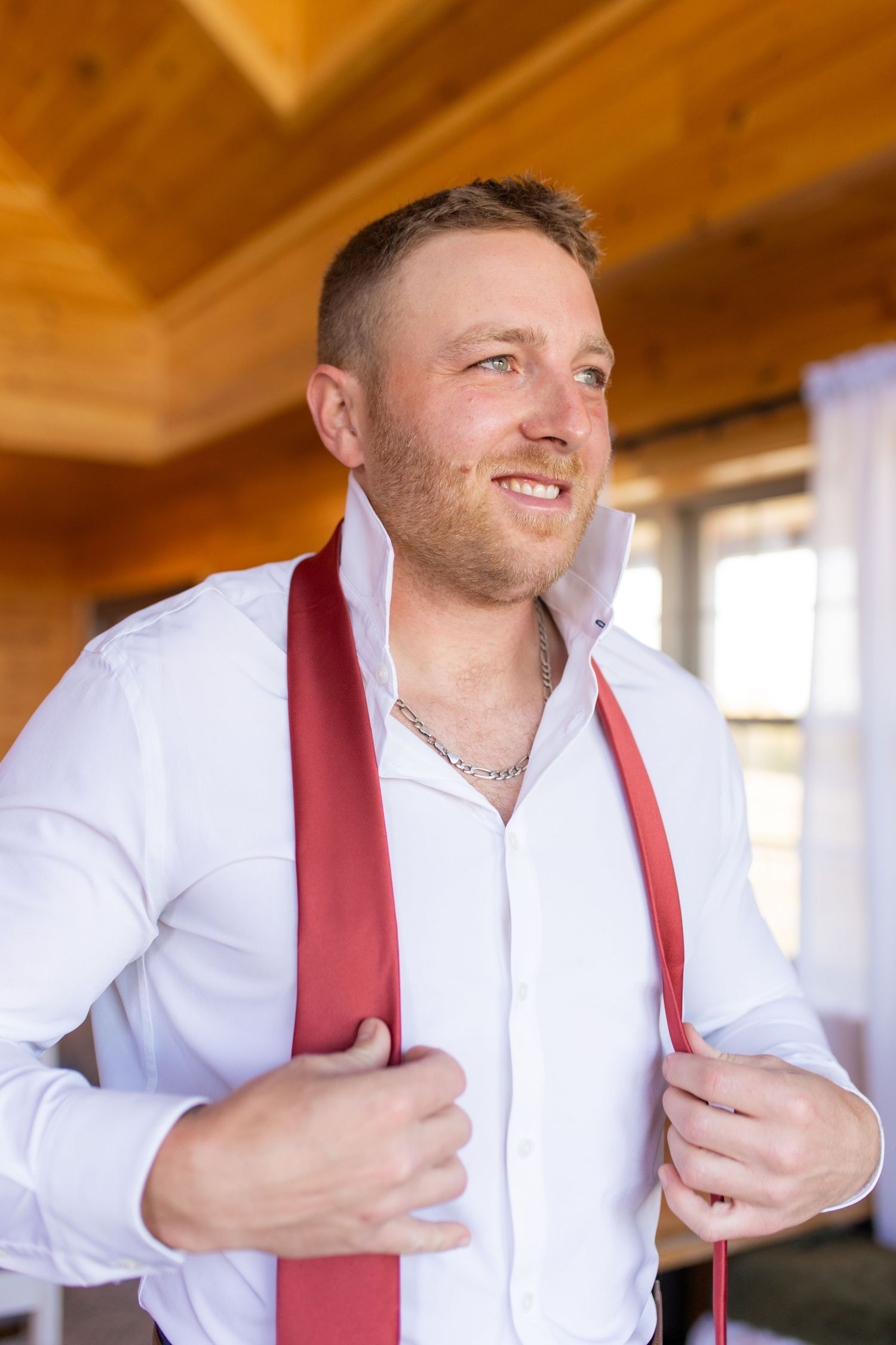 Sequence of groom adjusting red tie while getting ready in wooden room.