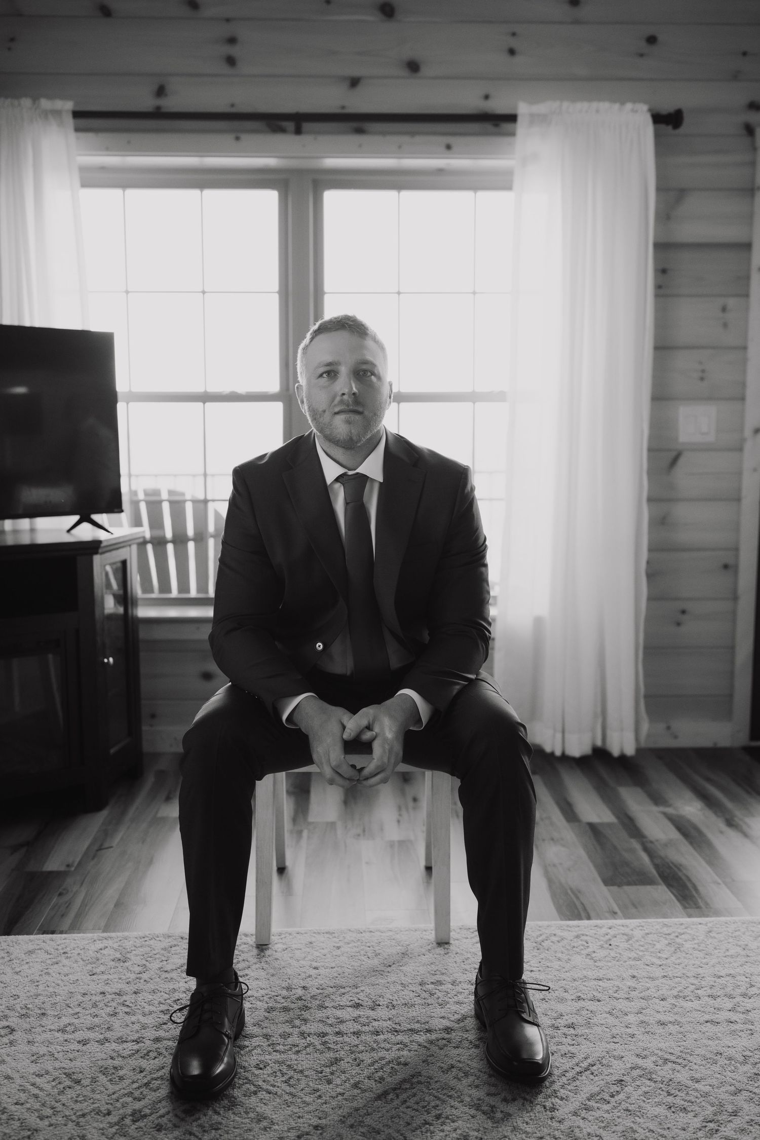 Black and white portrait series showing a suited figure seated in an empty room with natural light.