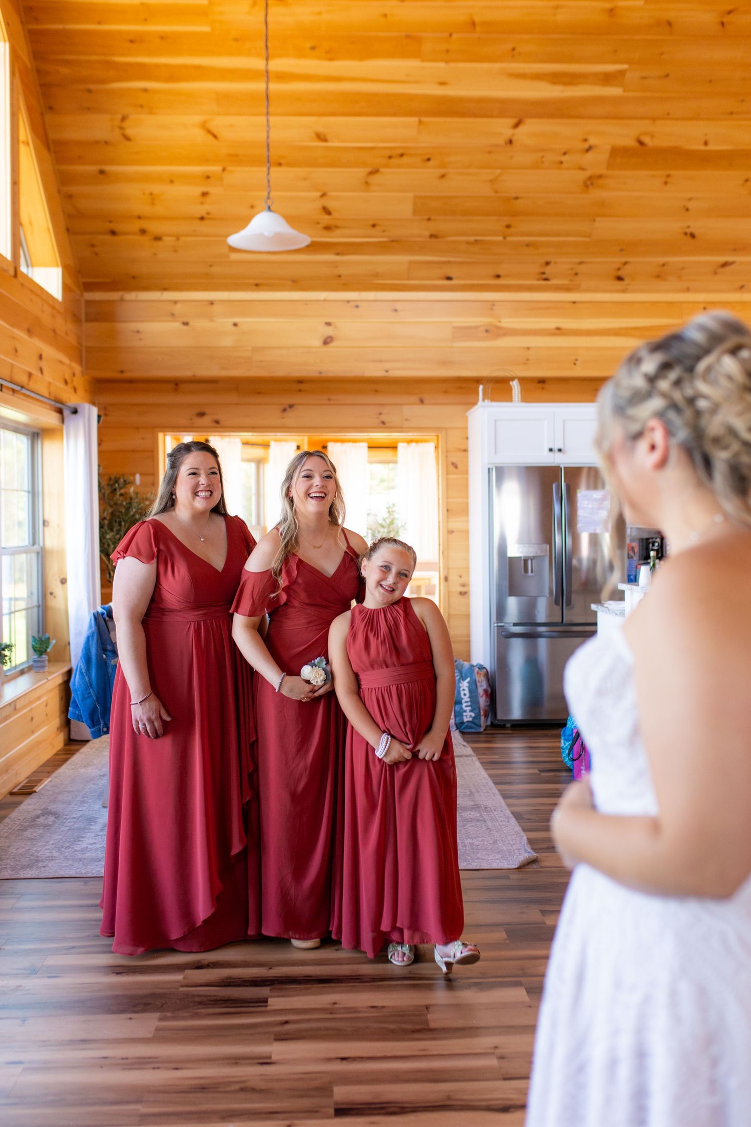 Bridesmaids in burgundy dresses standing together in a rustic wooden interior.