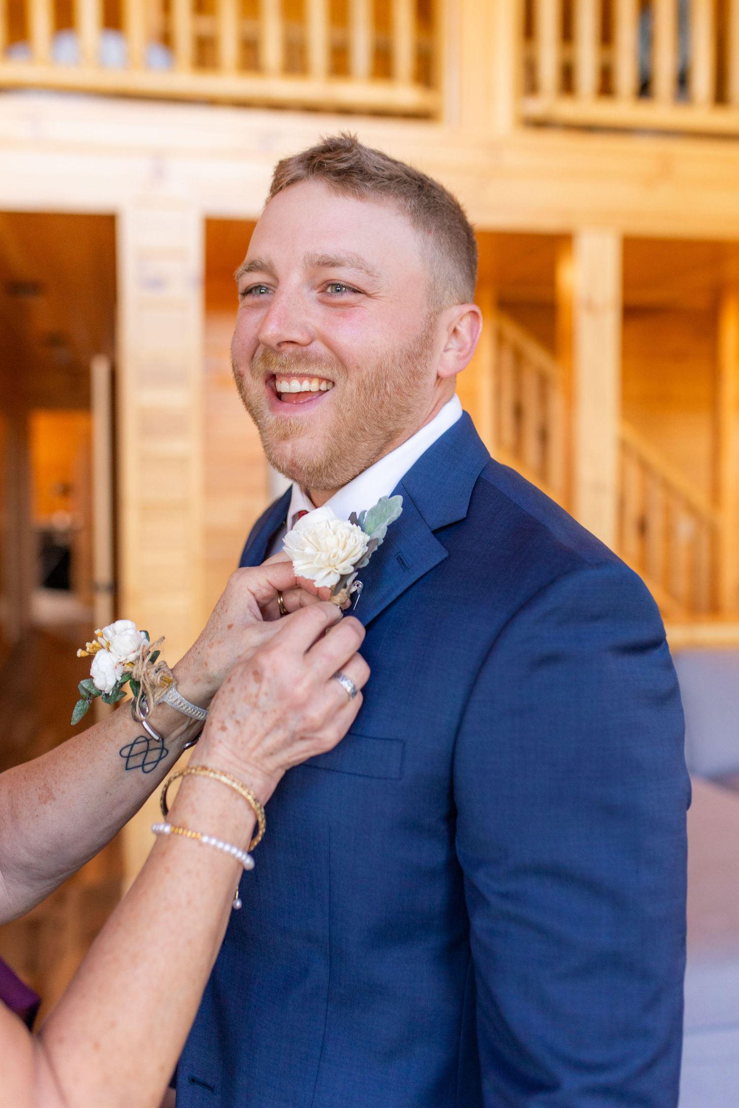 Someone helps adjust a boutonniere on a navy blue suit during wedding preparations.