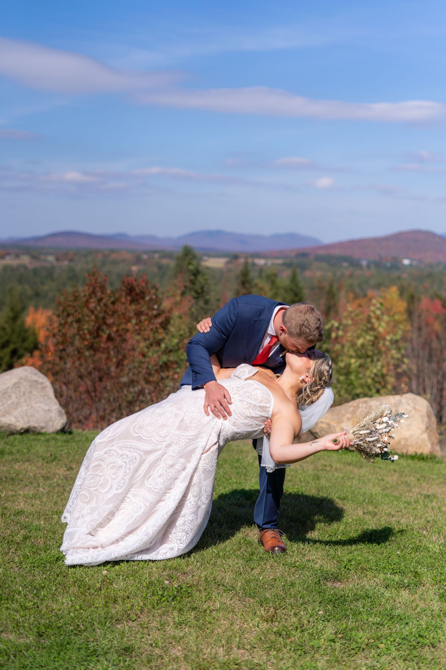 Romantic dip kiss between newlyweds with mountain vista in background.