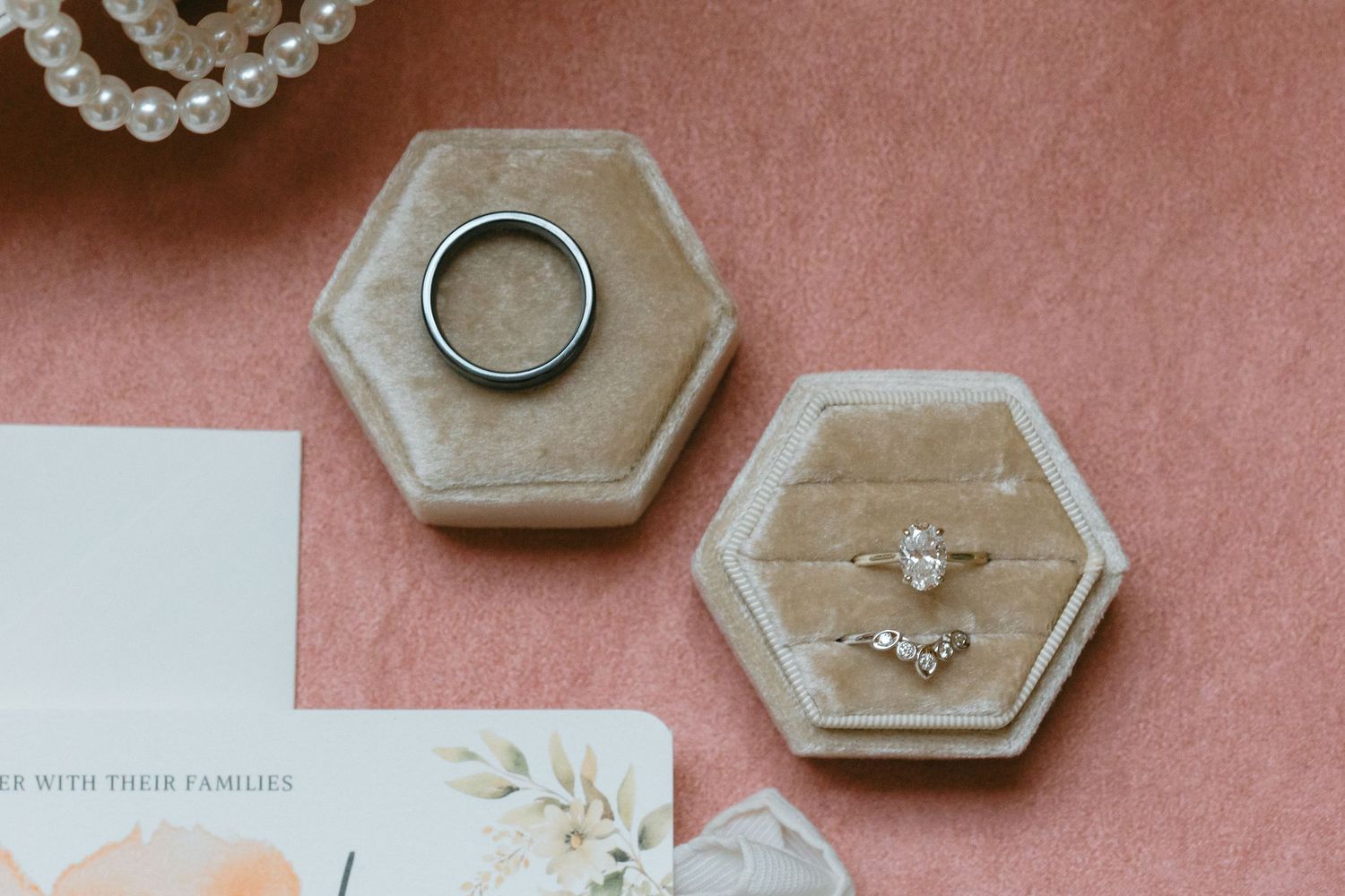 Wedding invitation suite with hexagonal ring dishes, floral stationery, and engagement rings on a pink background.