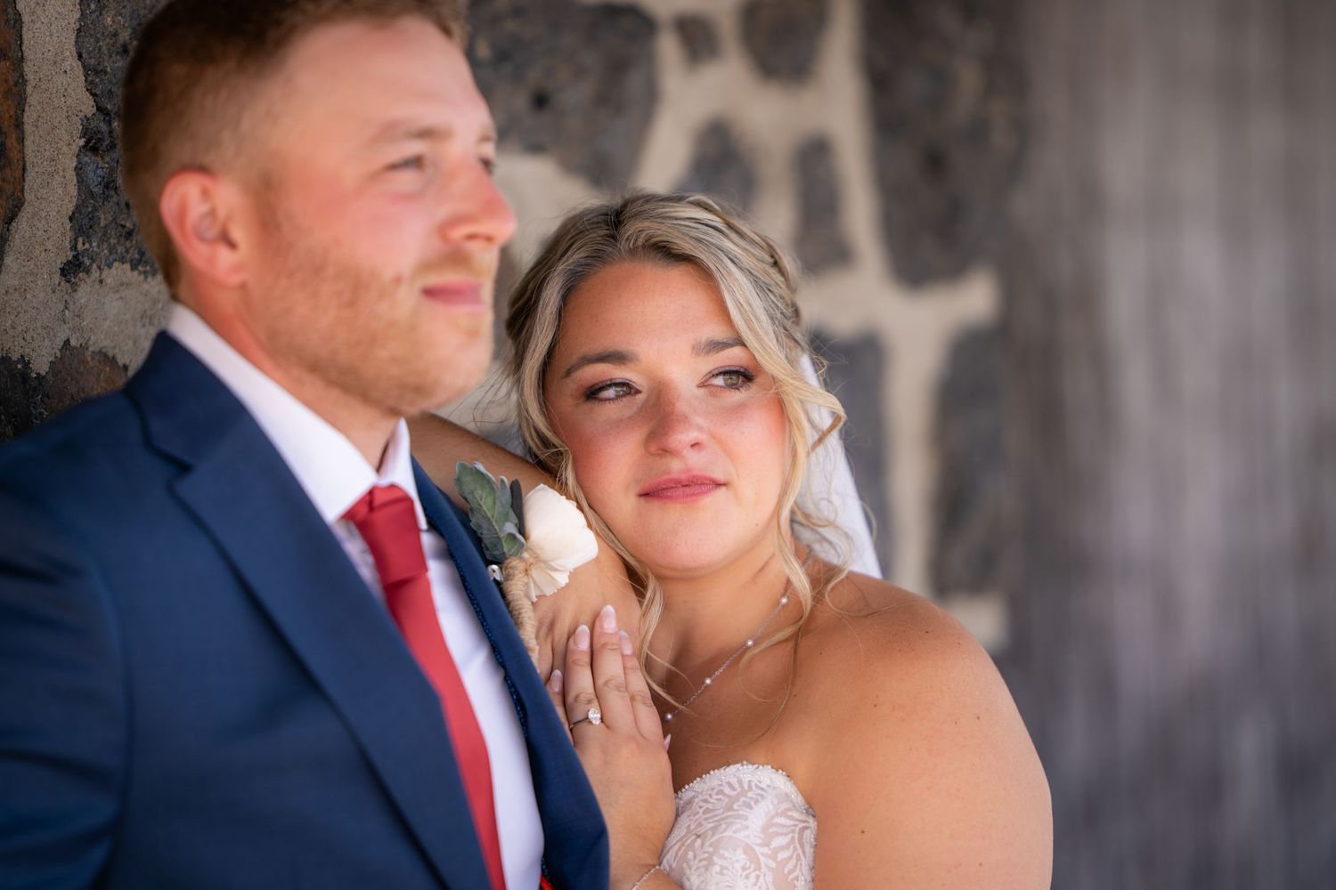 Wedding couple embracing outdoors against a textured wall background.