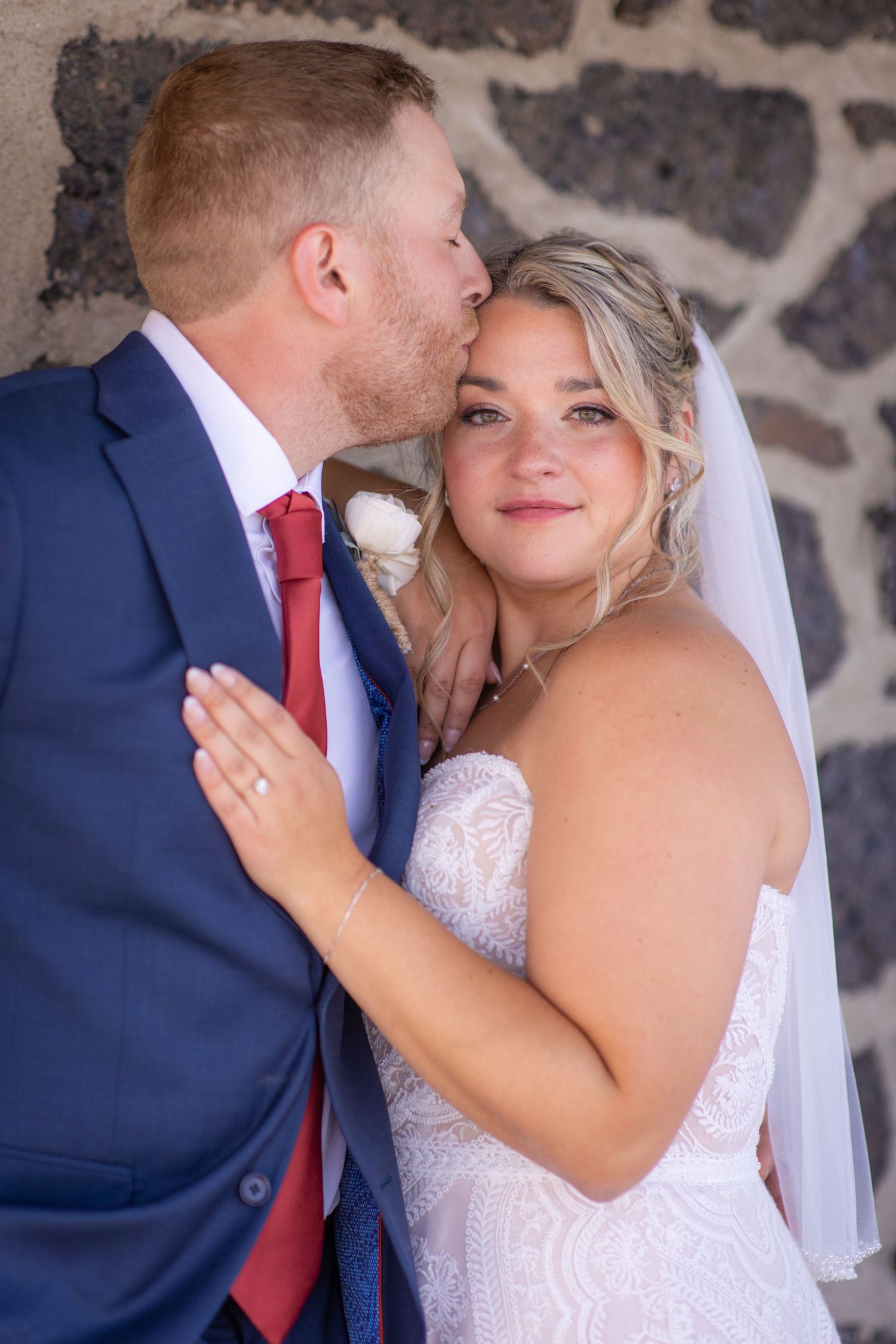Romantic wedding couple embracing against stone wall background.