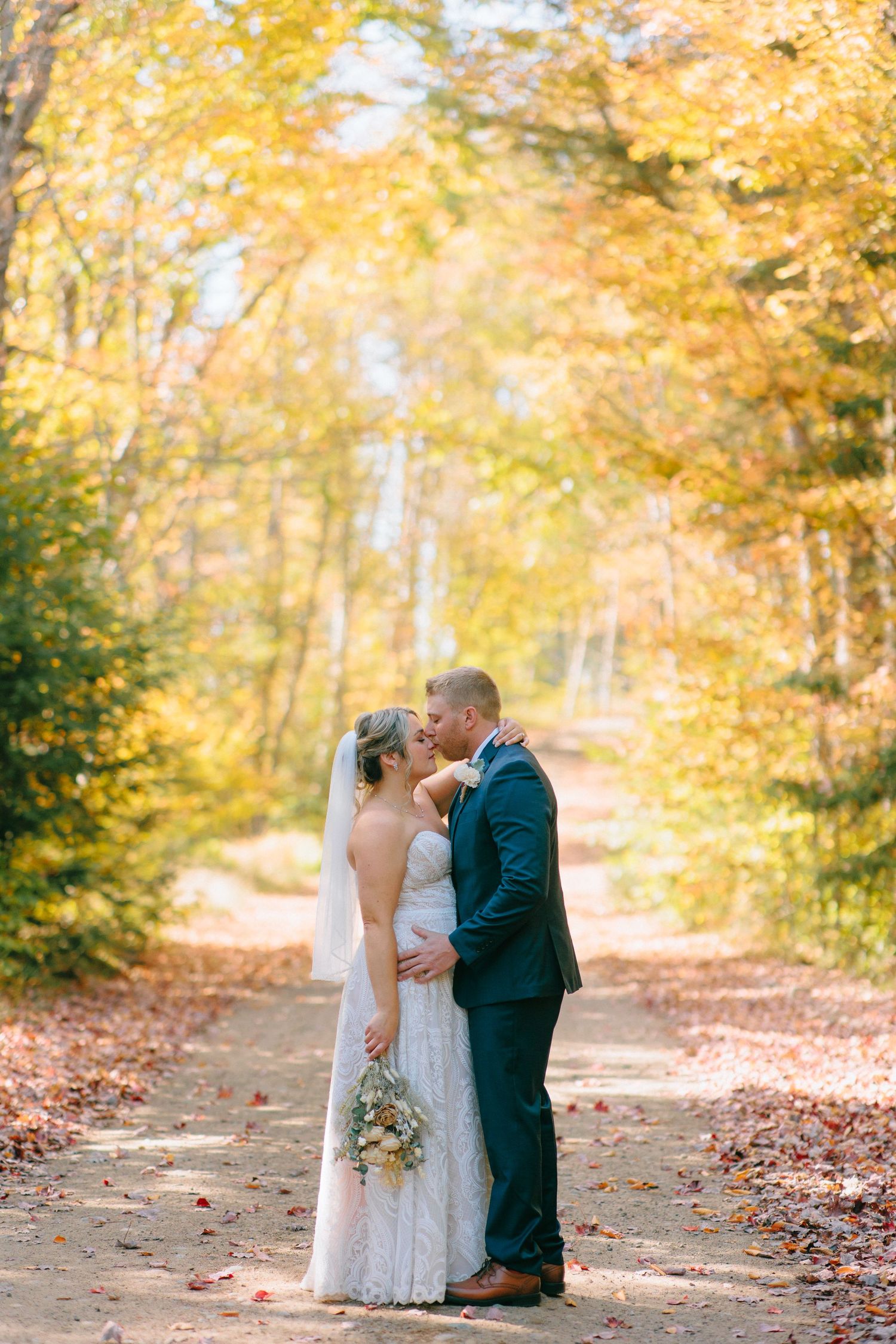 Romantic autumn wedding scene with golden leaves and a tree-lined path.