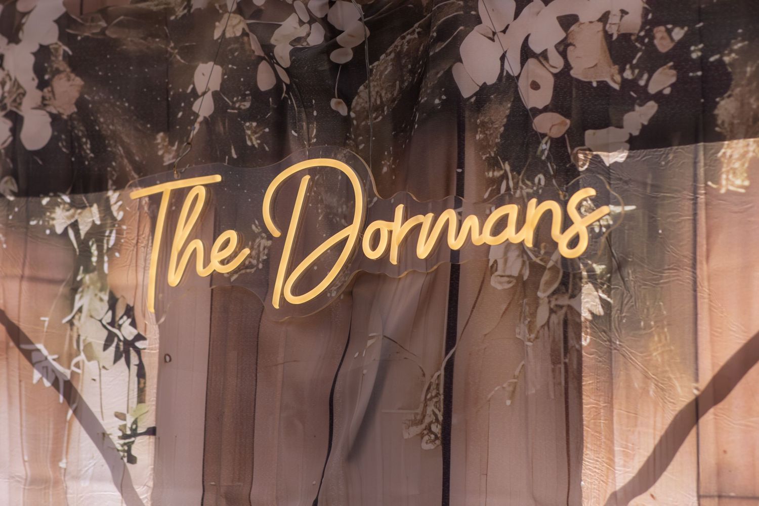 A rustic wooden sign with gold lettering spelling 'The Dormans' hangs against a white background with floral decor.