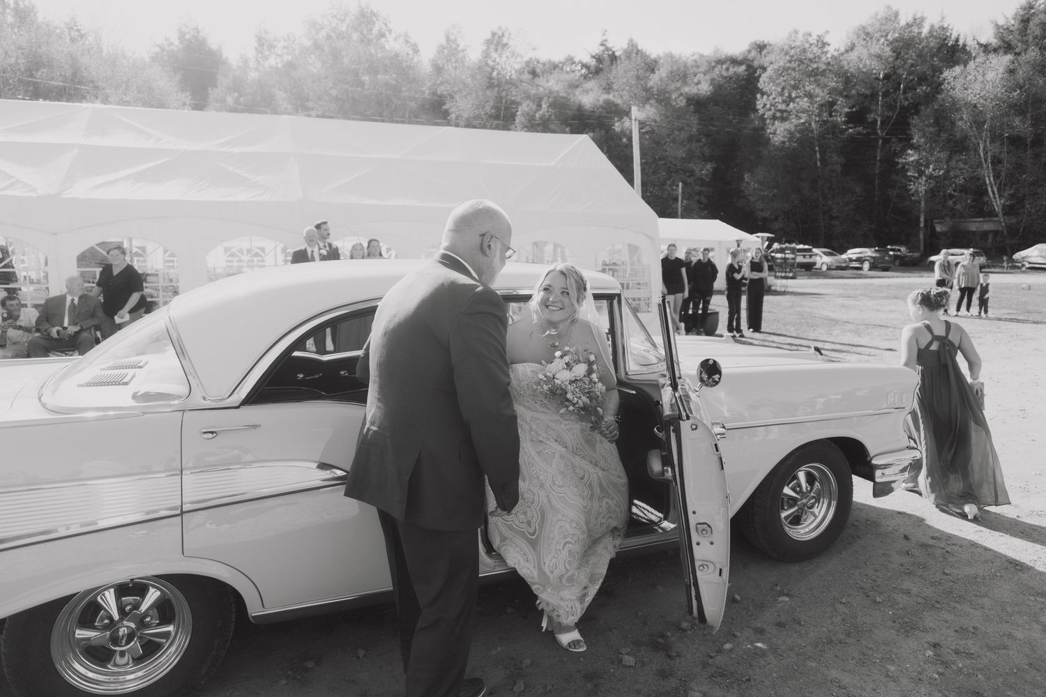 A classic white vintage car decorated for a wedding celebration with people gathering around it.