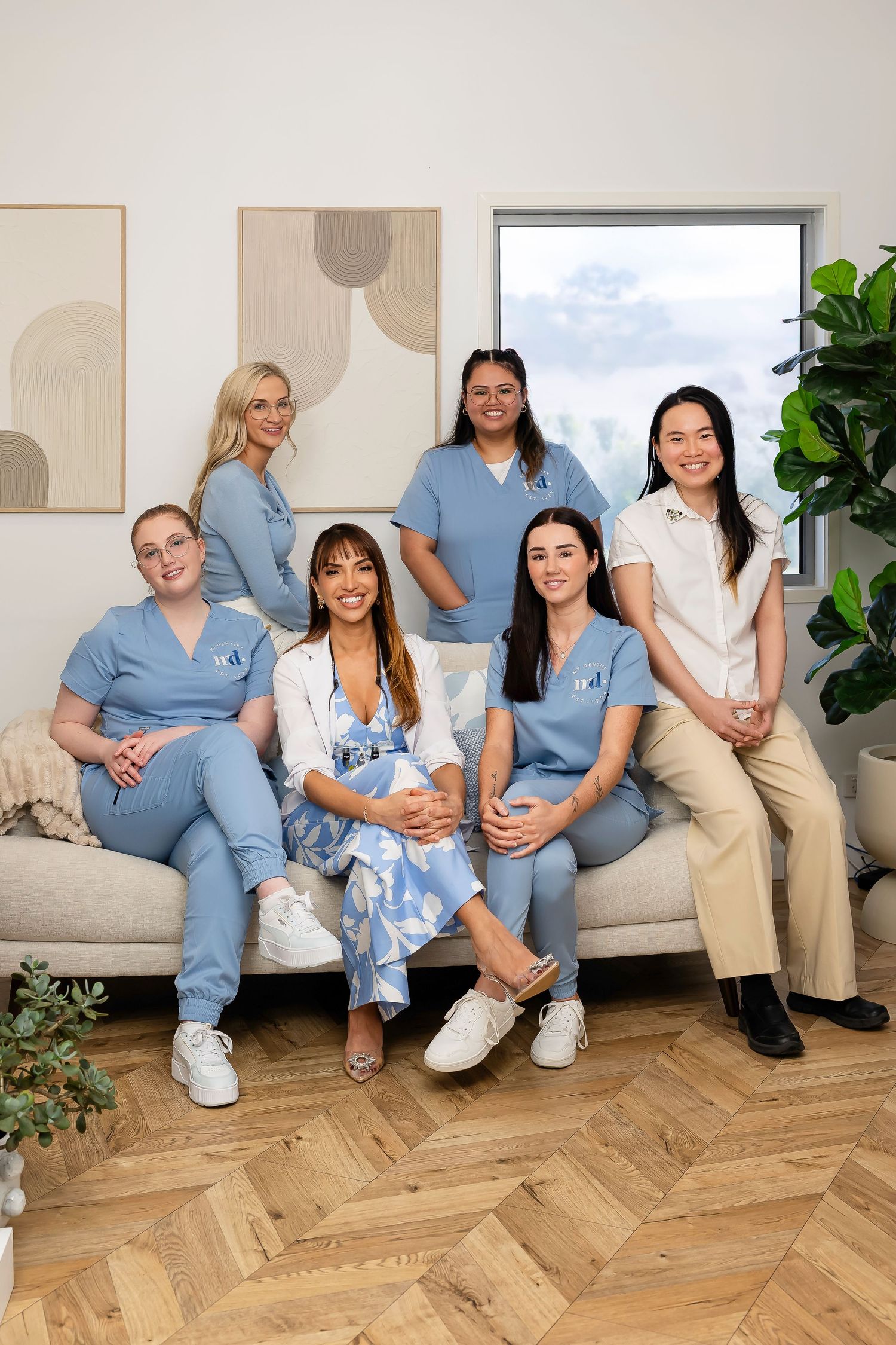 Healthcare professional in light blue scrubs and glasses smiling warmly at the camera.