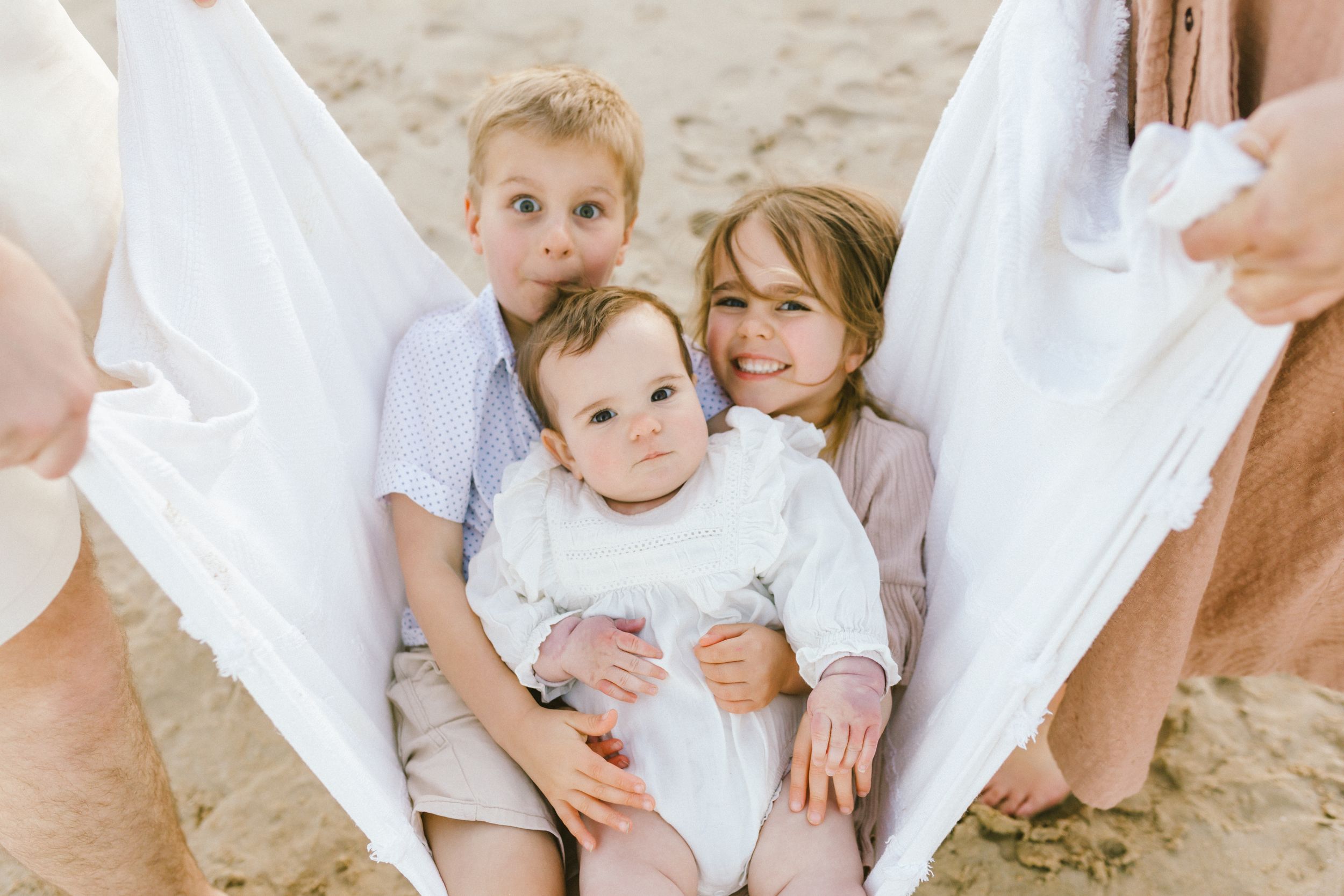 Family wearing white outfits sits together on sandy beach during sunset photo session.
