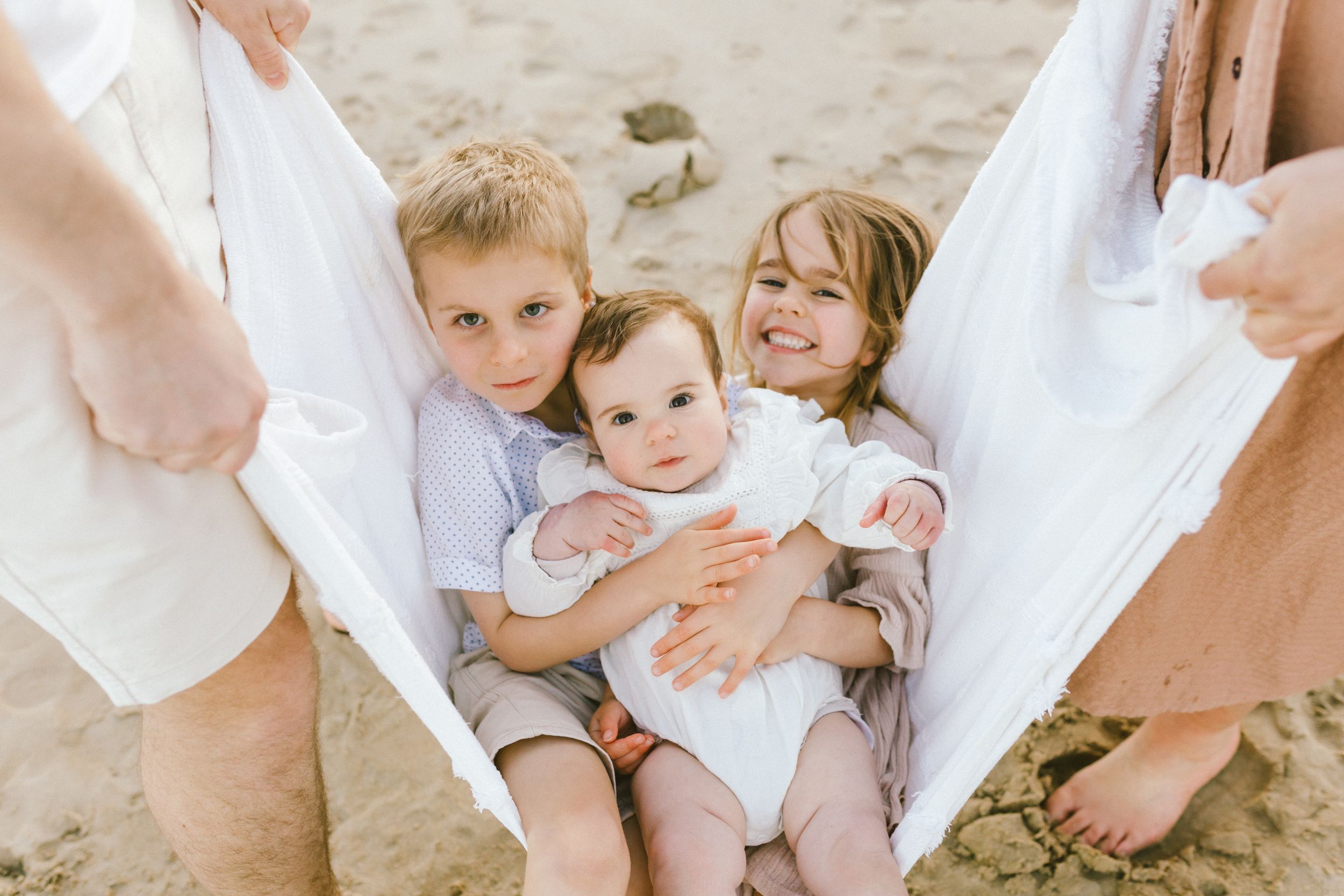 Family members in white clothing gather on beach sand during golden hour photography.