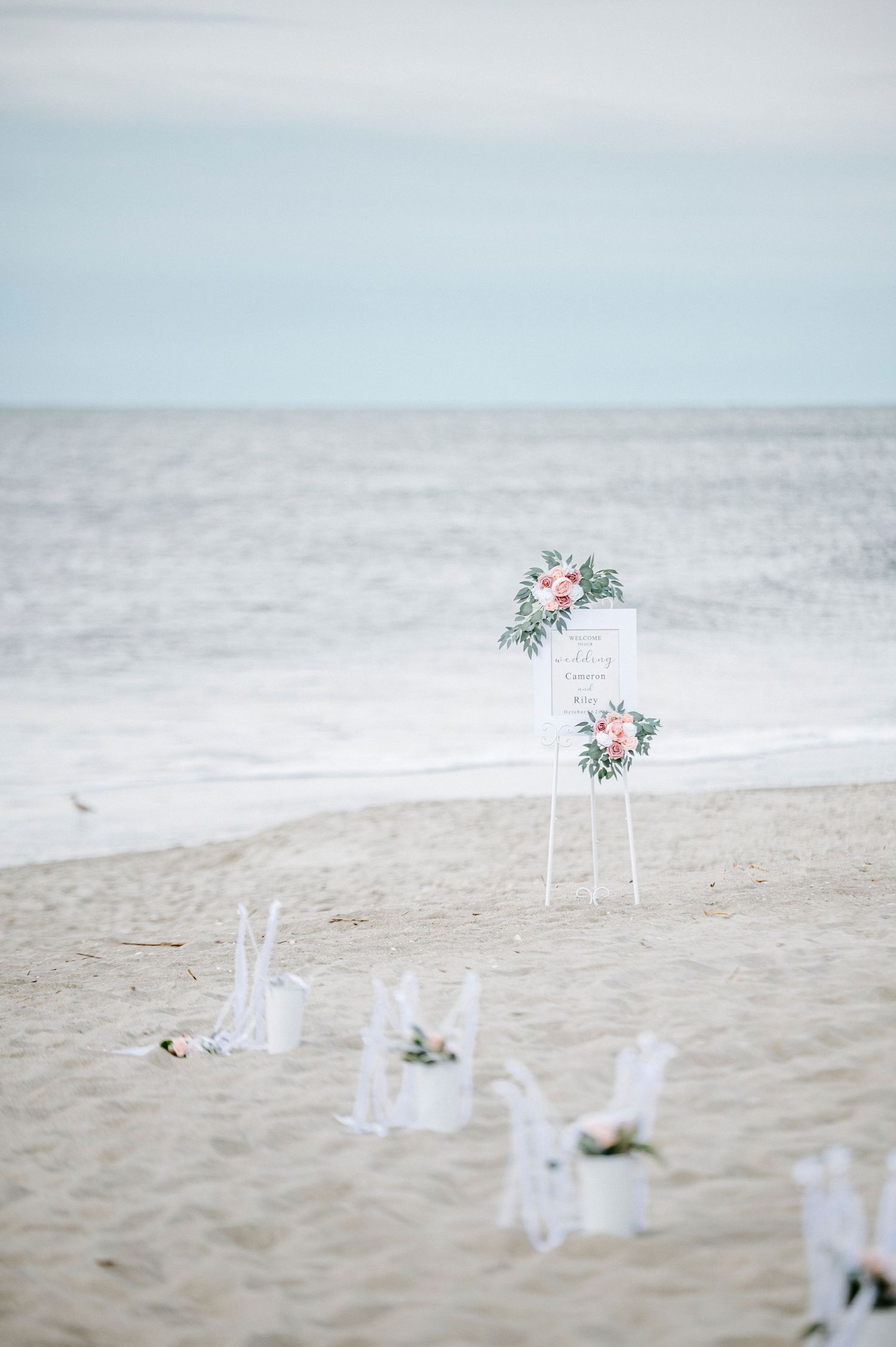 White chairs and floral arrangements set up for a romantic beach wedding ceremony with ocean views.