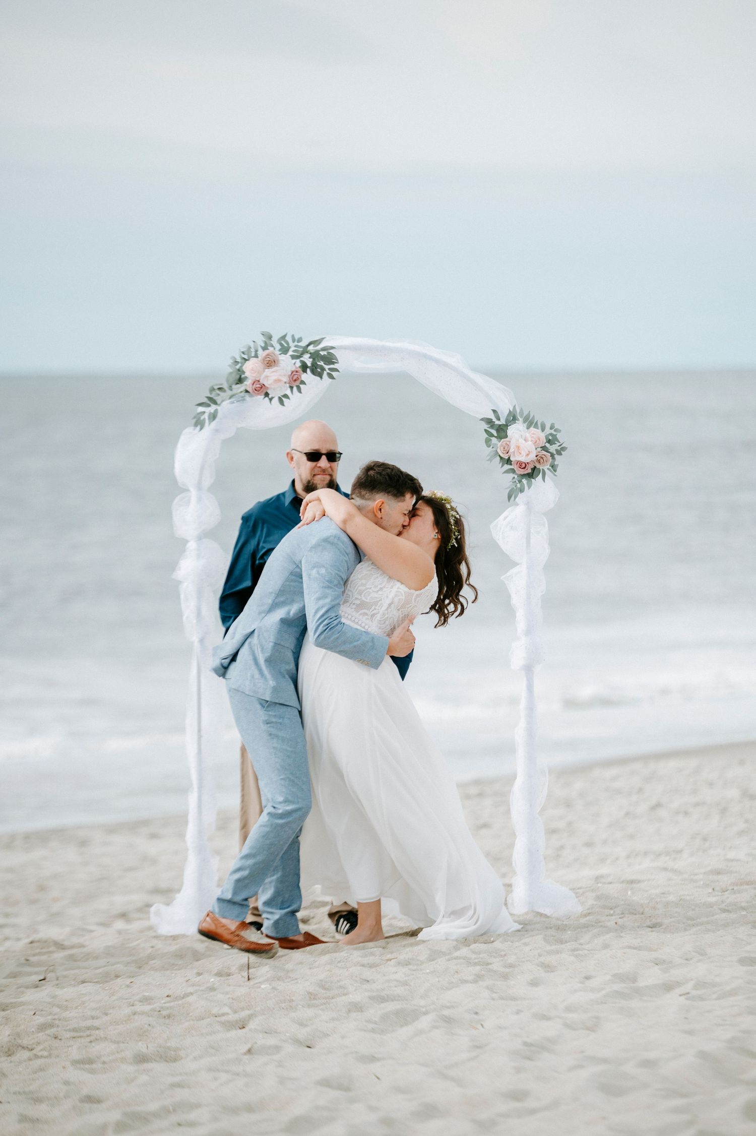 A romantic beach wedding ceremony with a white arch and floral decorations along the shoreline.