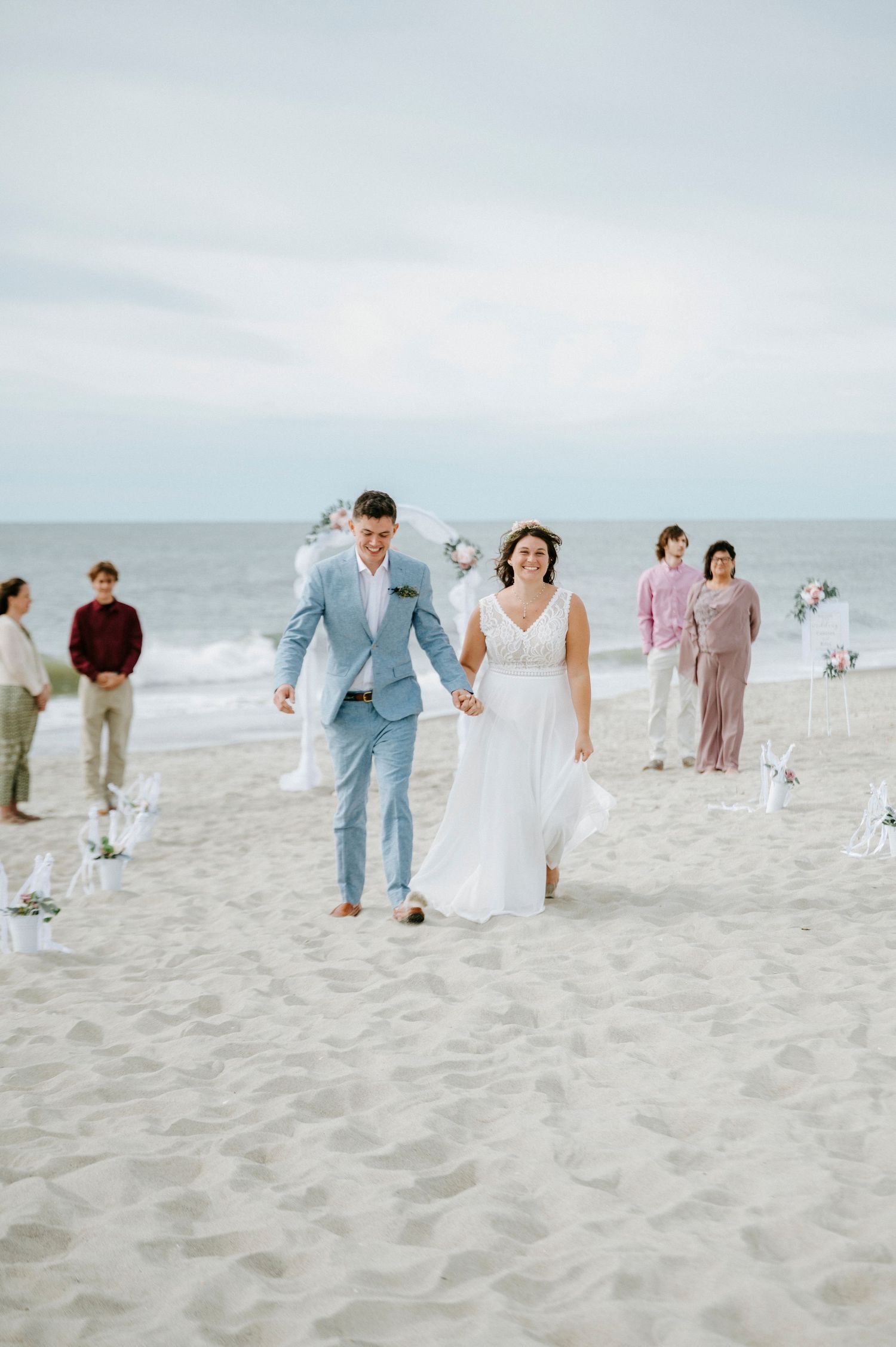 Wedding party walking along a sandy beach with the ocean in the background on an overcast day.