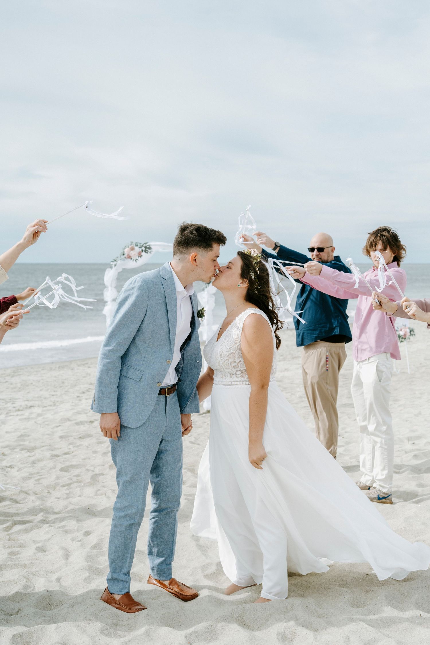 Wedding party celebrates joyfully on a sunny beach with streamers flying through the air.