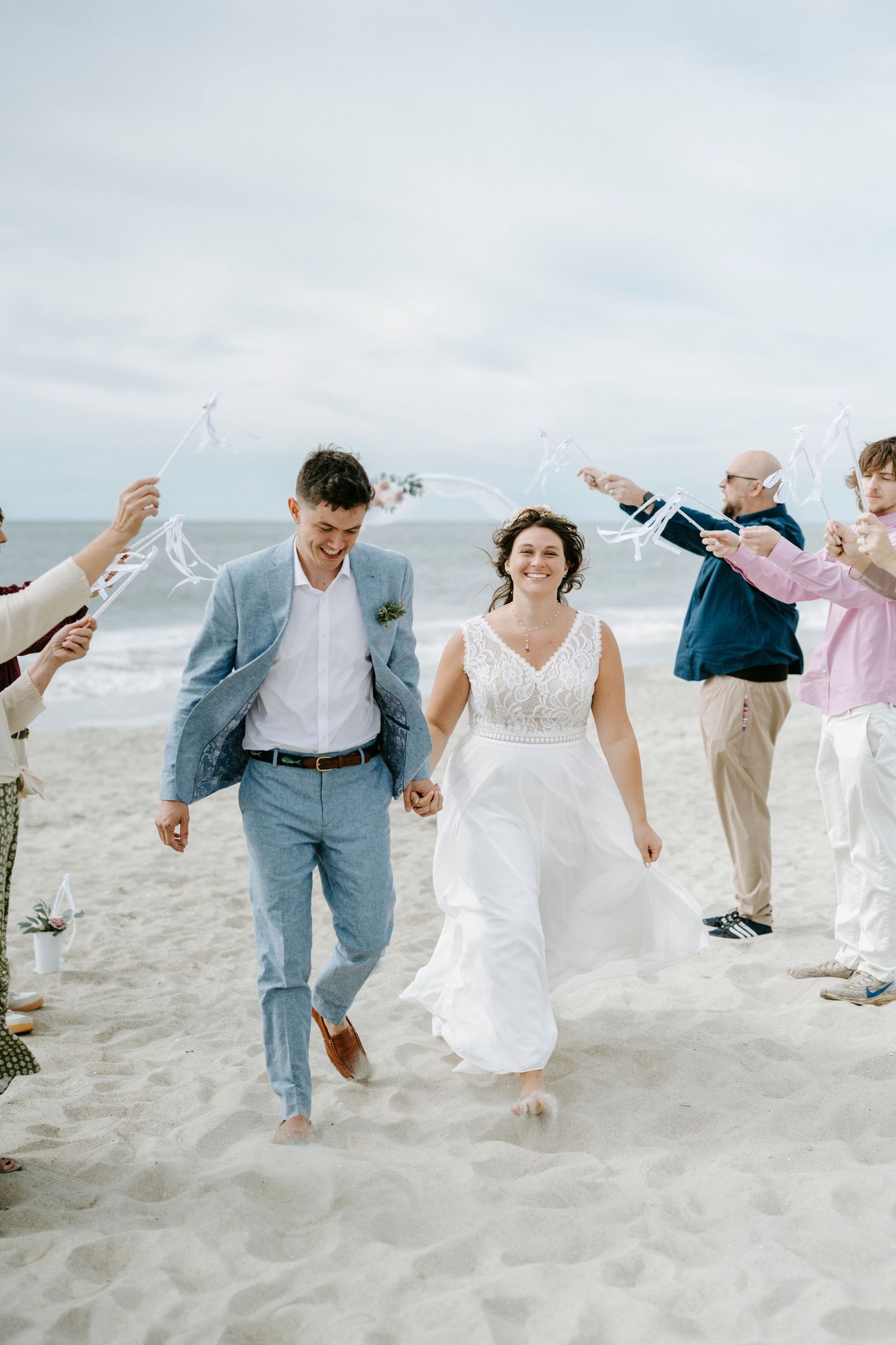 Wedding party jumps joyfully together on a cloudy beach, creating a fun and candid moment.