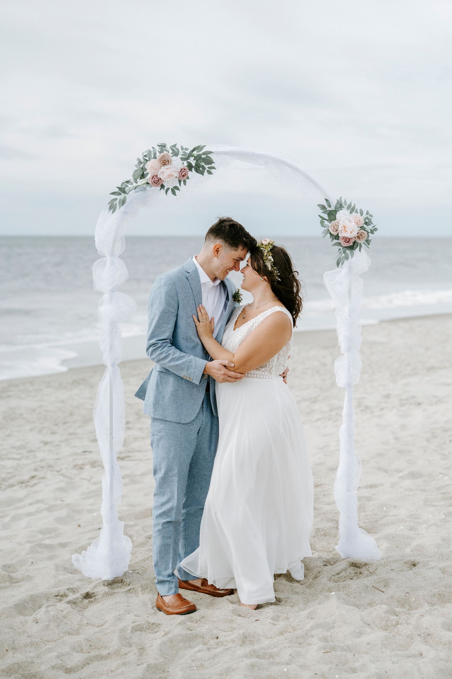 Romantic beach wedding ceremony with floral arch and couple sharing an intimate moment on the sand.