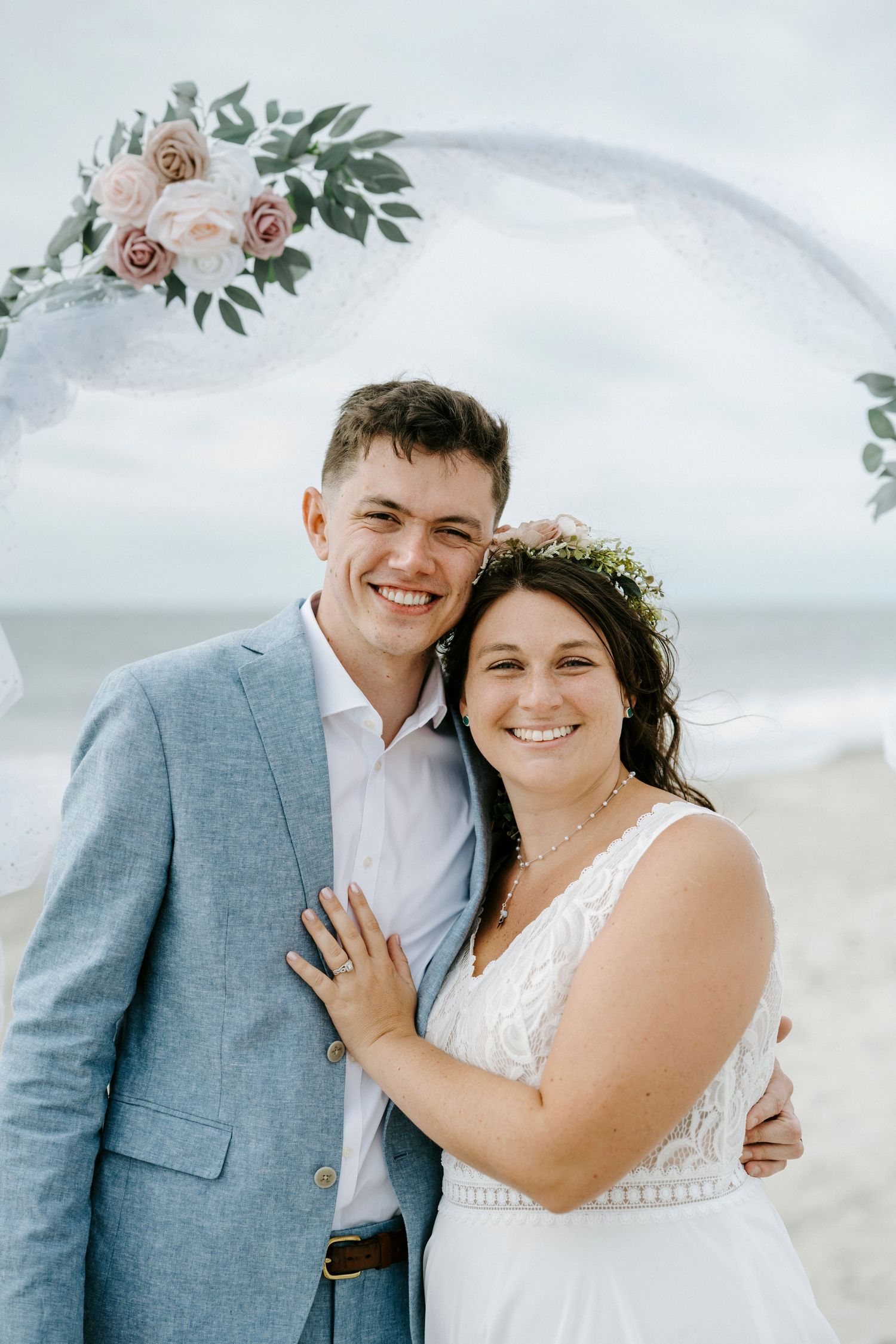 Newlyweds share a joyful moment under a floral arch during their beach wedding ceremony.