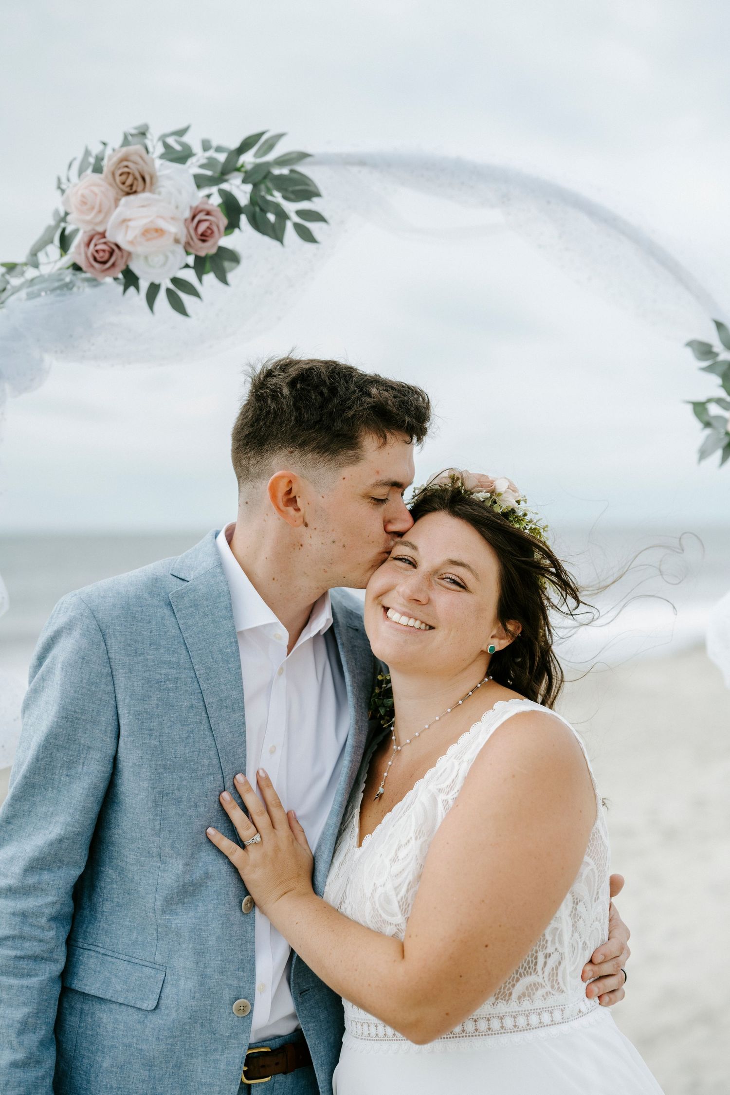 A romantic beach wedding moment with a couple embracing under a floral arch against an ocean backdrop.