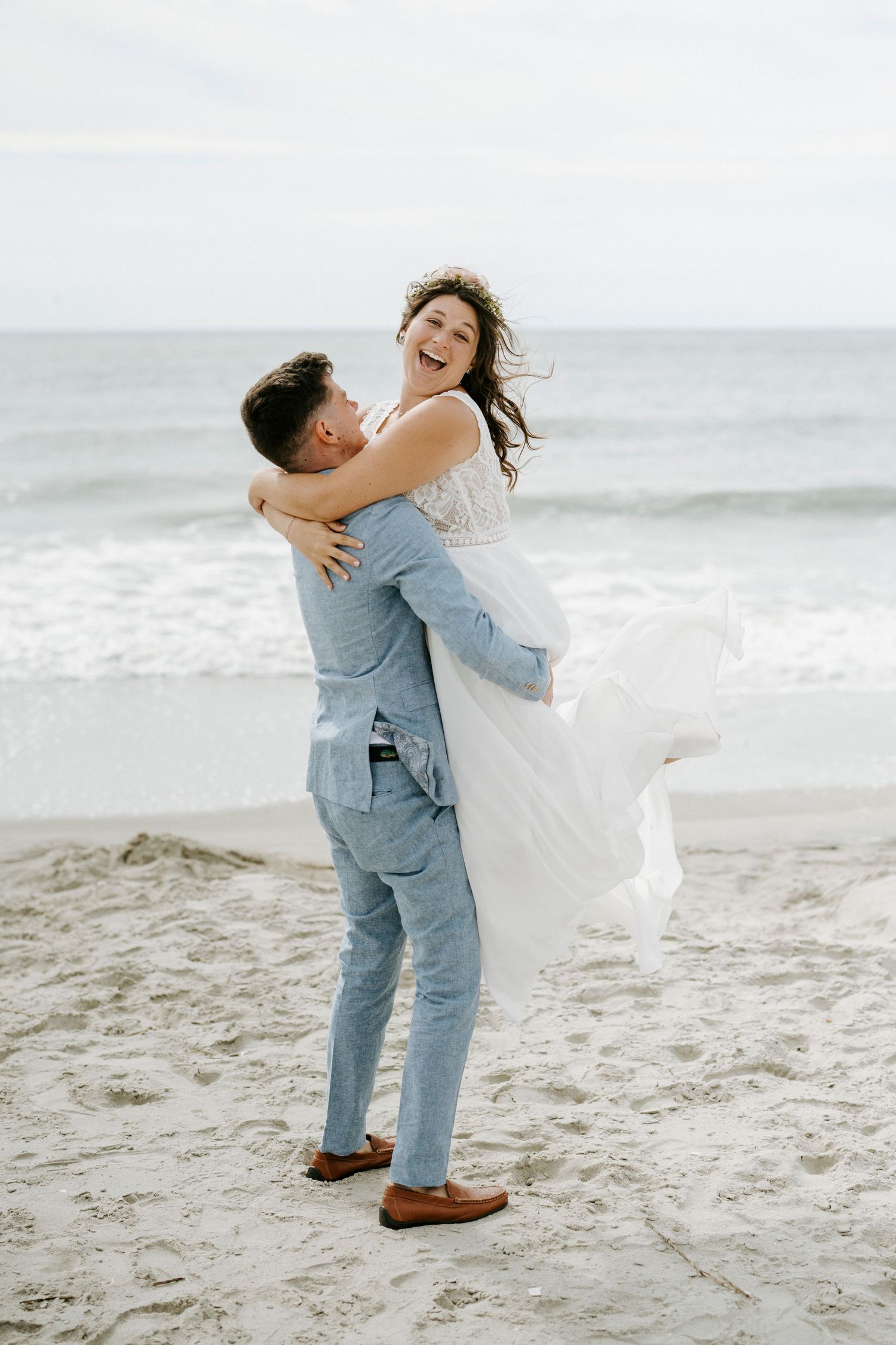 Couple shares playful lifts and embraces during their beach wedding photoshoot.
