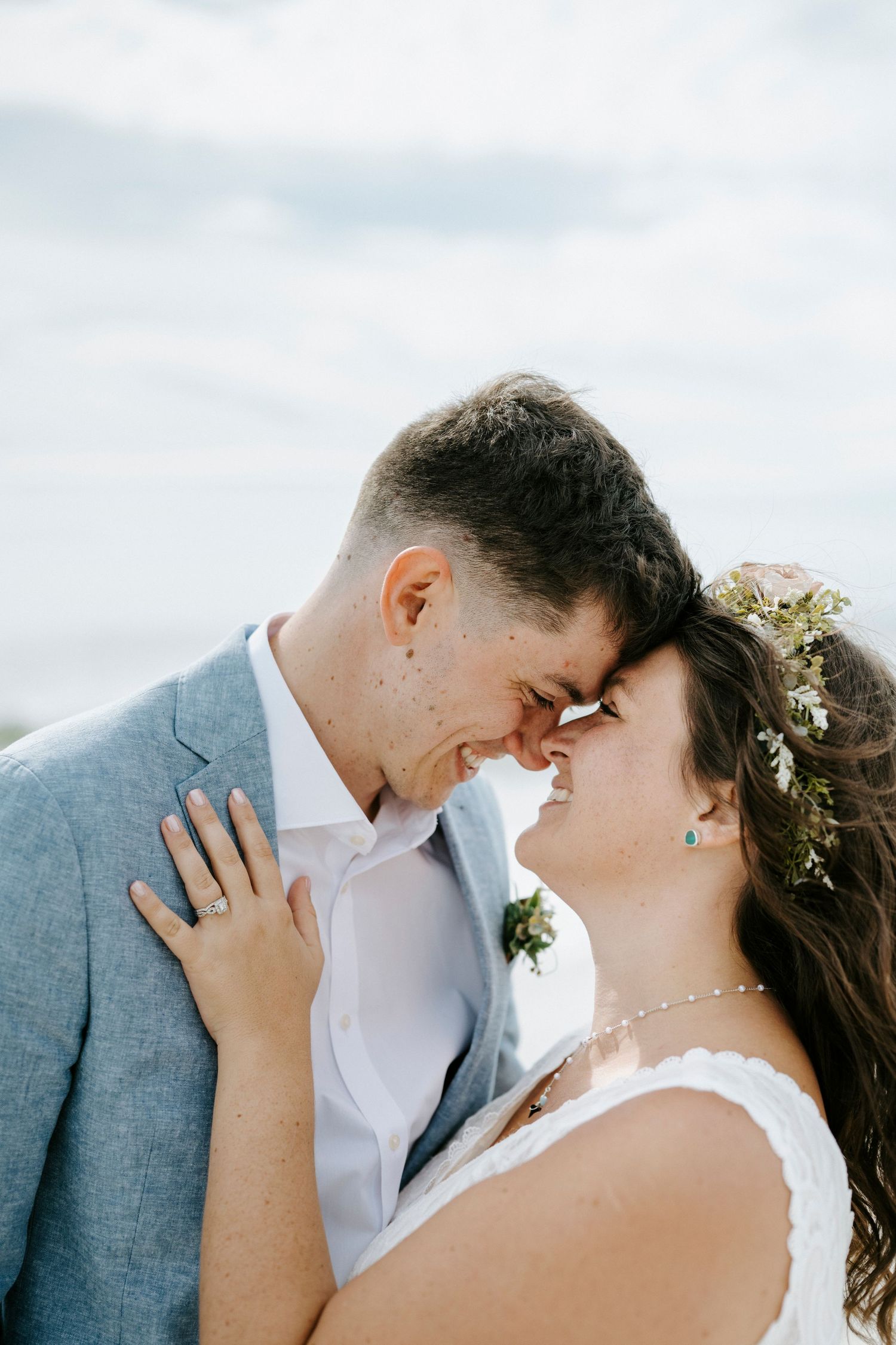 An intimate wedding portrait showing a tender moment between newlyweds on a coastal beach setting.
