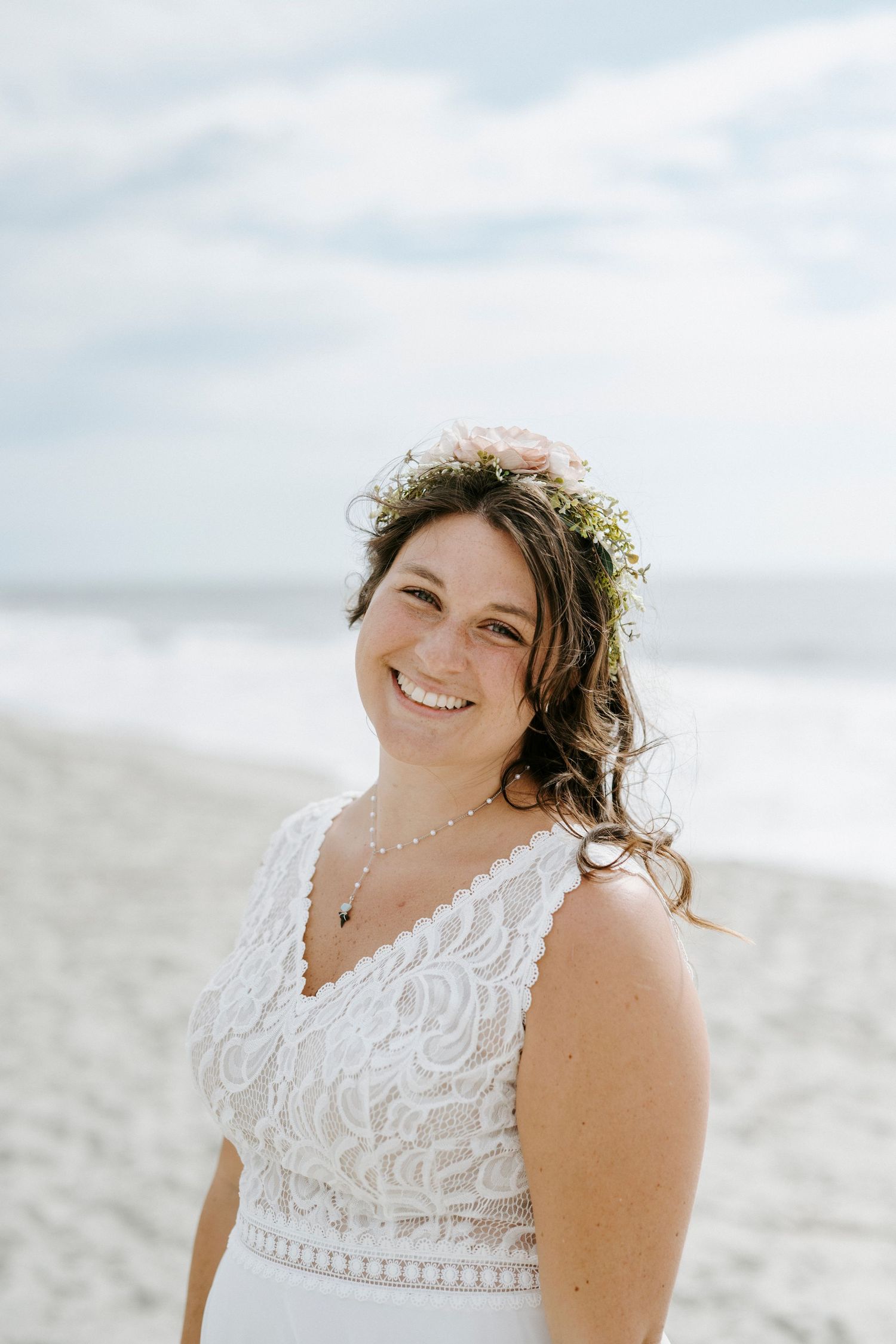 Bride with flower crown smiles radiantly during beach wedding photoshoot.