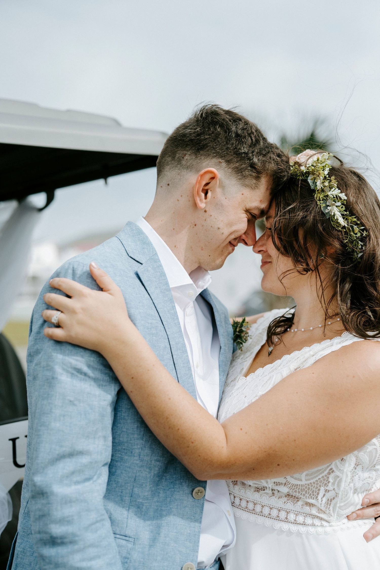 A romantic wedding couple shares an intimate moment together, the bride wearing a floral crown and lace dress.
