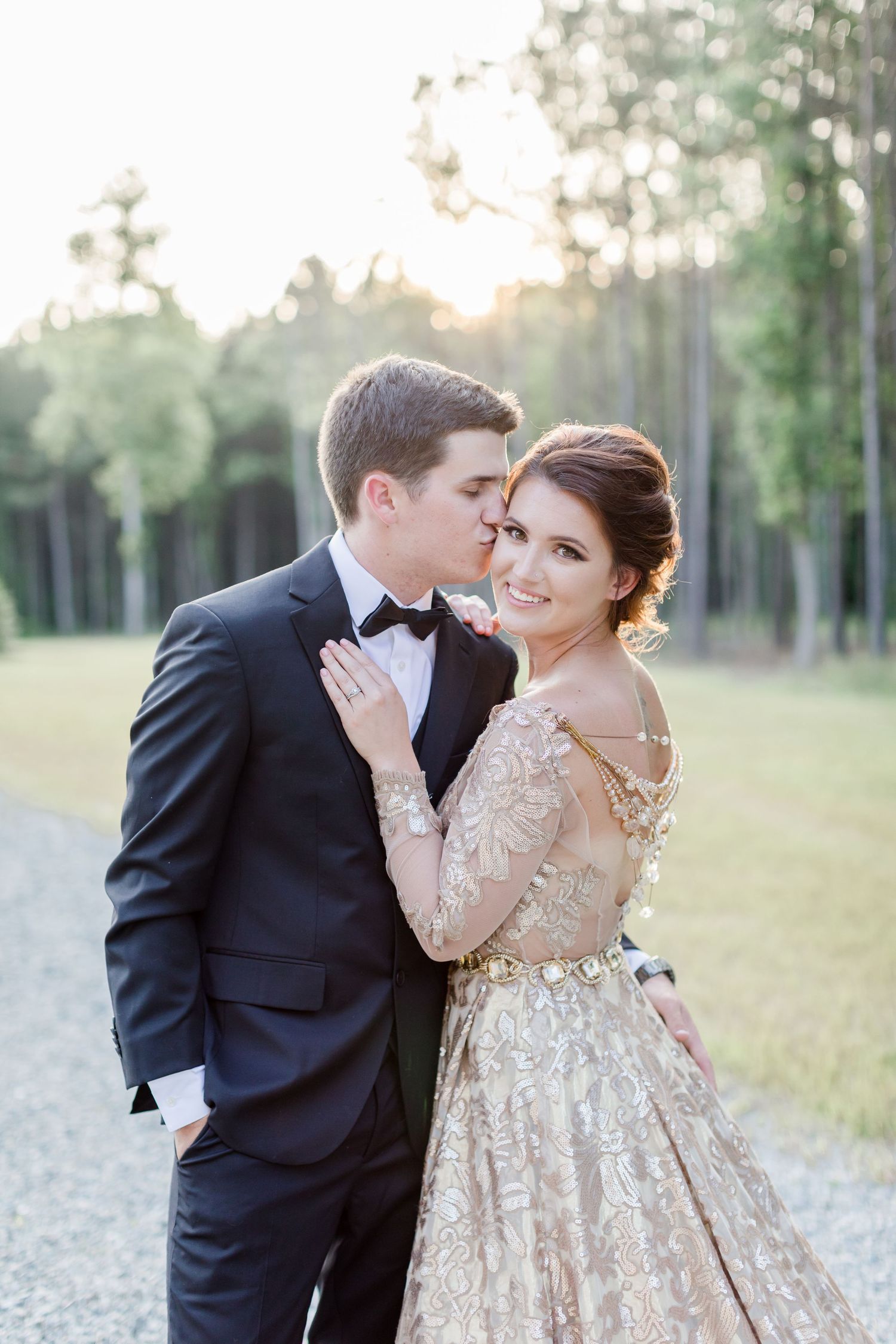 Romantic couple in formal wear sharing intimate moments in an outdoor field at sunset.