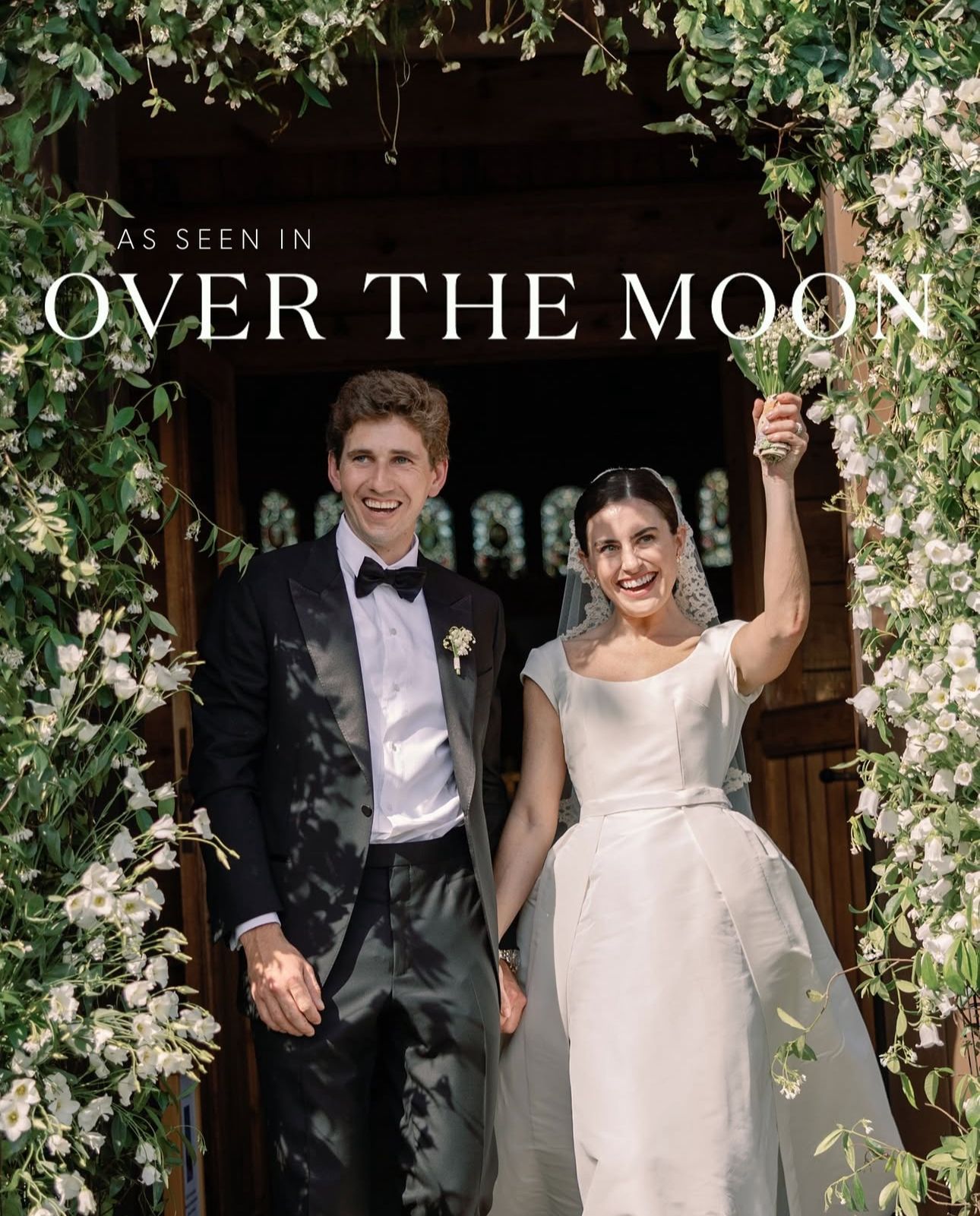 Newlywed couple celebrates joyfully under a floral arch decorated with white blossoms at their wedding ceremony.