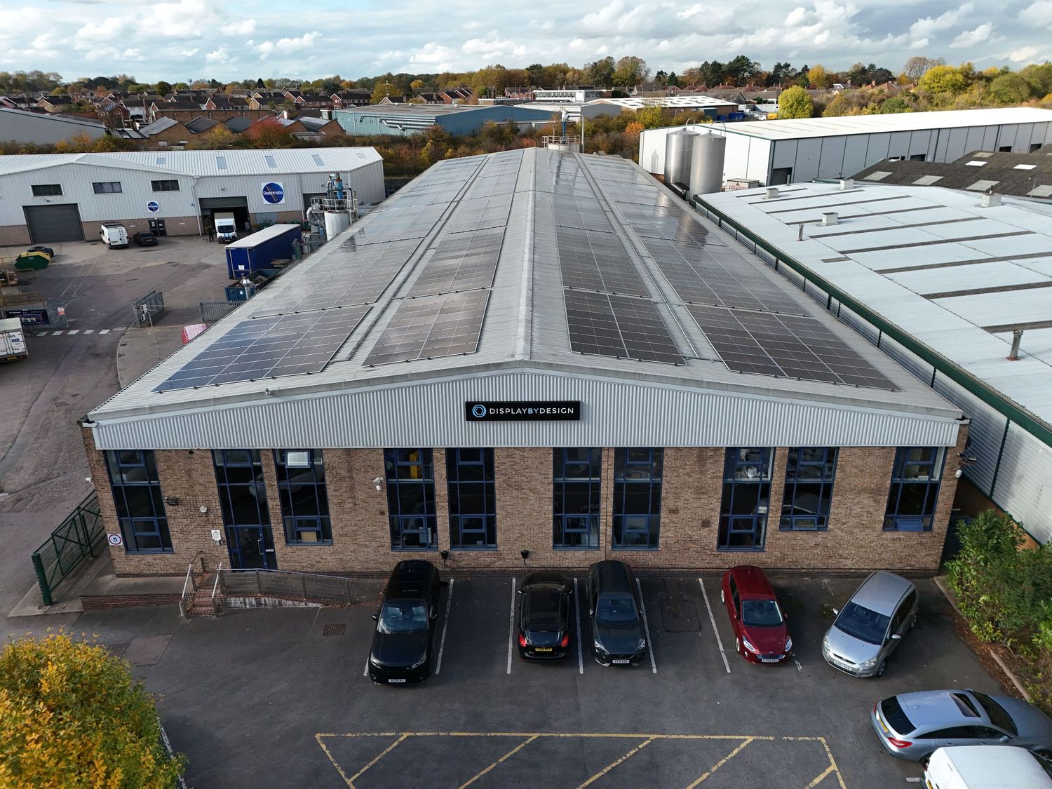 Modern commercial office building complex with parked cars and landscaping visible from an aerial perspective.