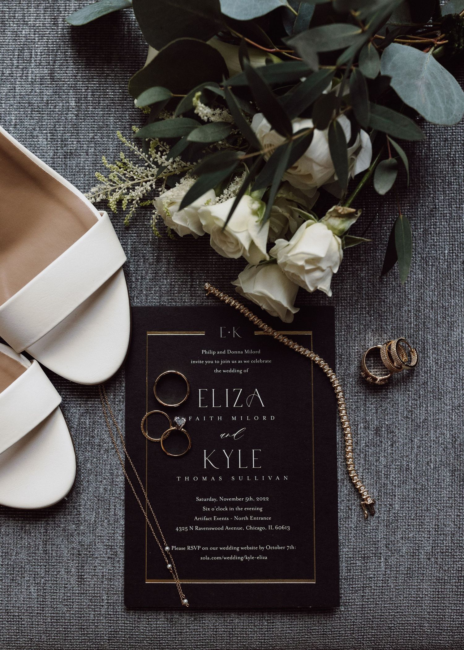 Black and gold wedding invitations with floral decorations displayed on a gray textured surface.