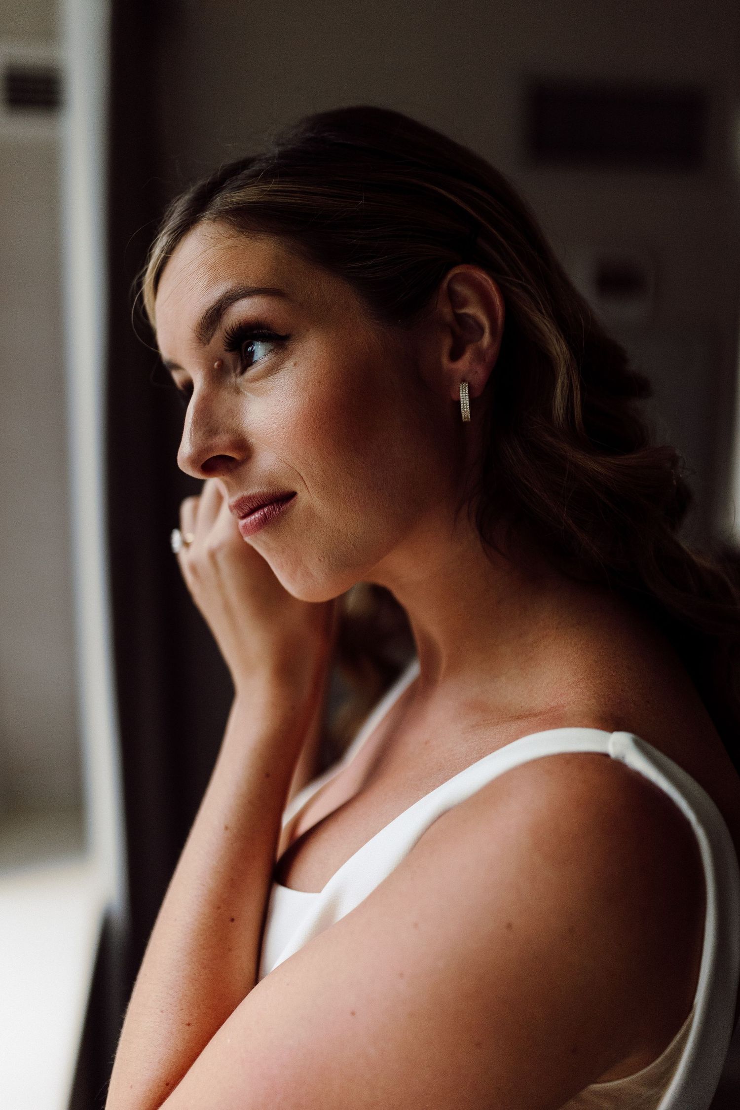 Woman in white dress sitting by window in soft natural light.