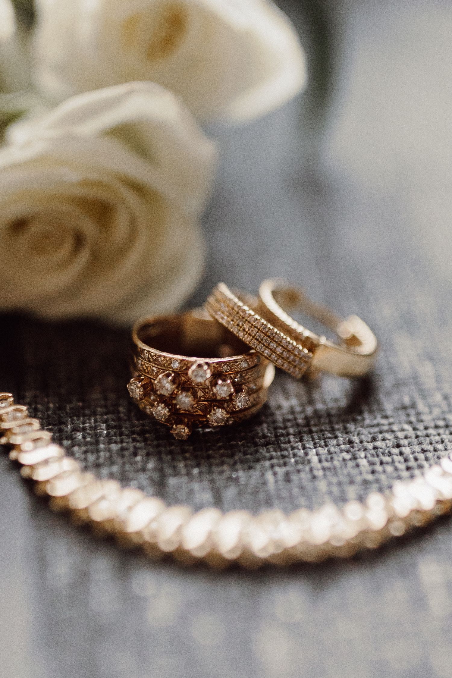 Rose gold wedding rings and jewelry arranged on a textured gray fabric with delicate details.