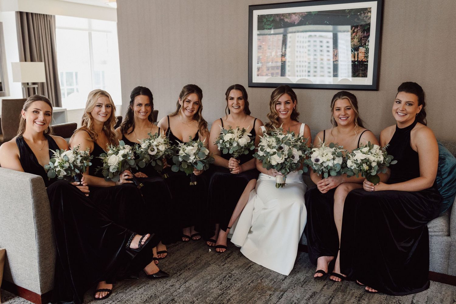 Wedding party group photo with bridesmaids in black dresses holding white floral bouquets.