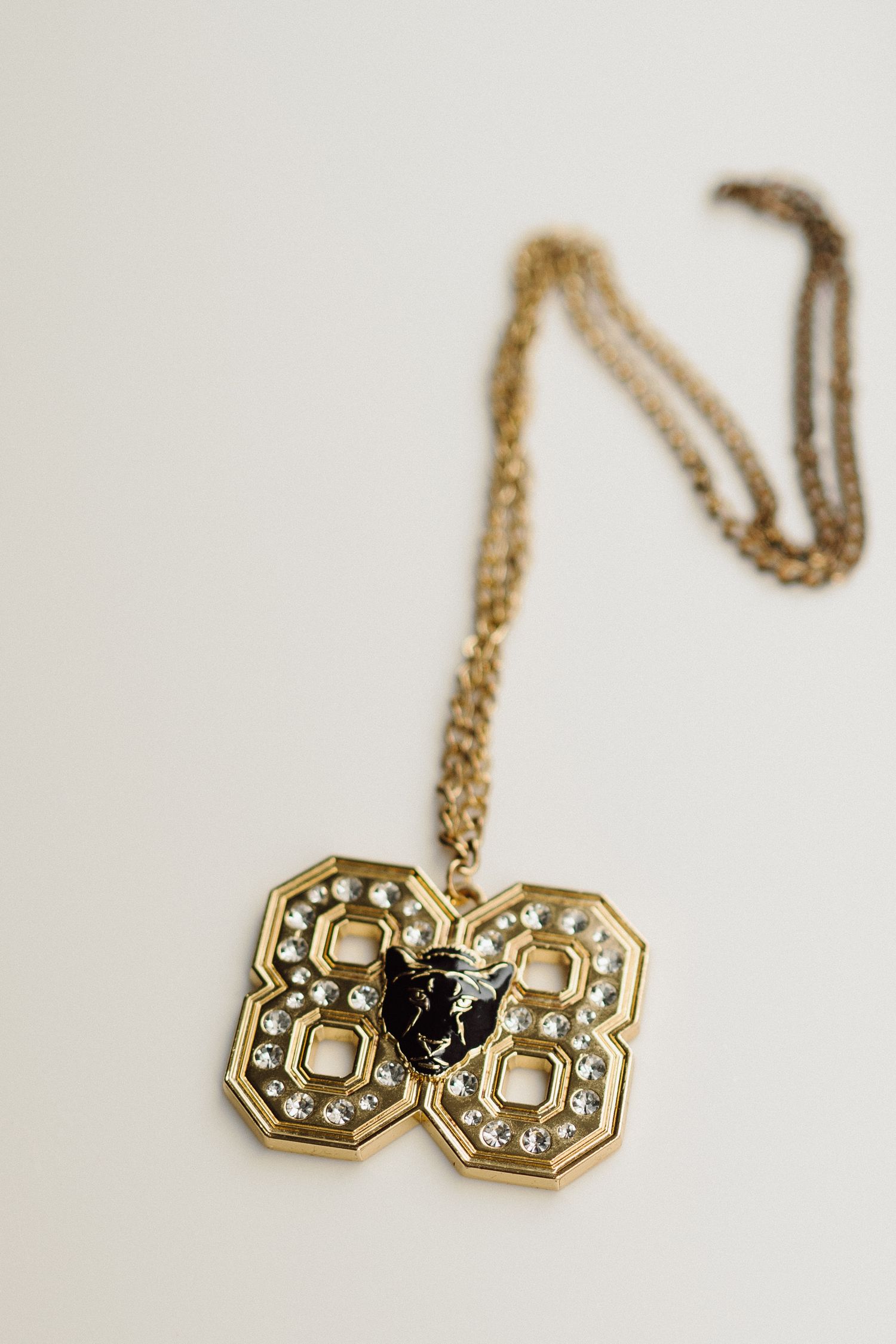 Gold vintage-style necklace with geometric pendant and crystal details on white background.