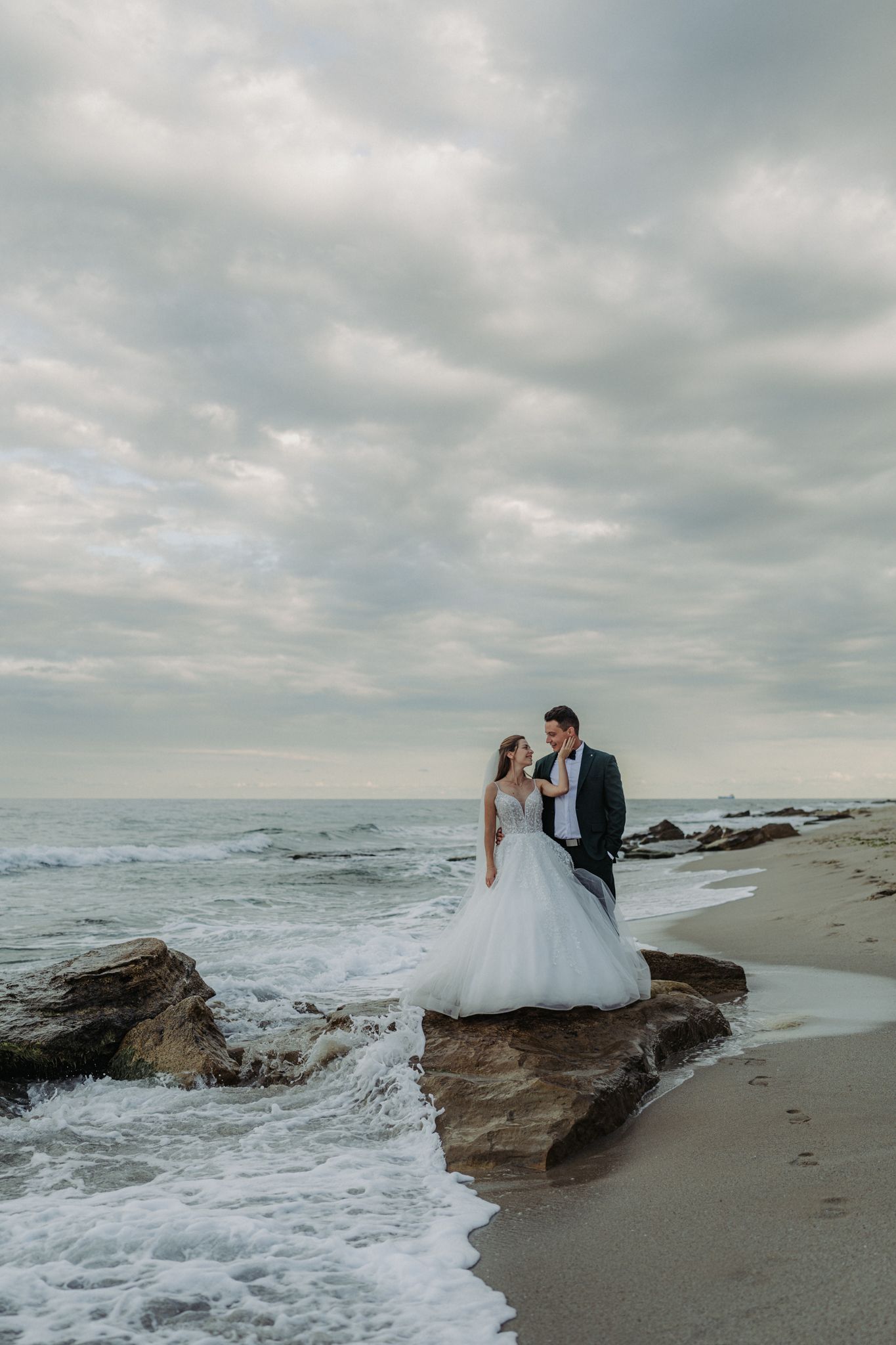 A romantic beach wedding moment with a couple embracing on the sand as stormy clouds gather overhead.