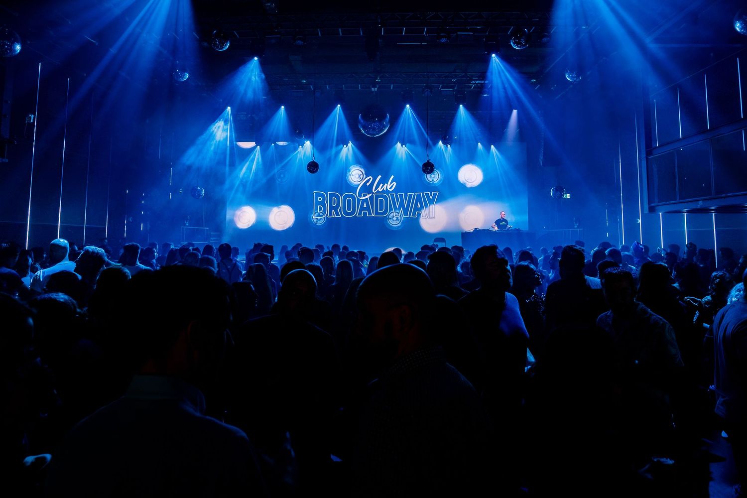 Silhouetted crowd at concert venue with dramatic blue stage lighting and fog effects.