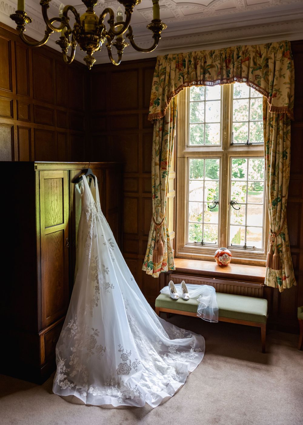 A stunning white wedding dress with lace details and long train displayed in a rustic wooden room with chandelier.