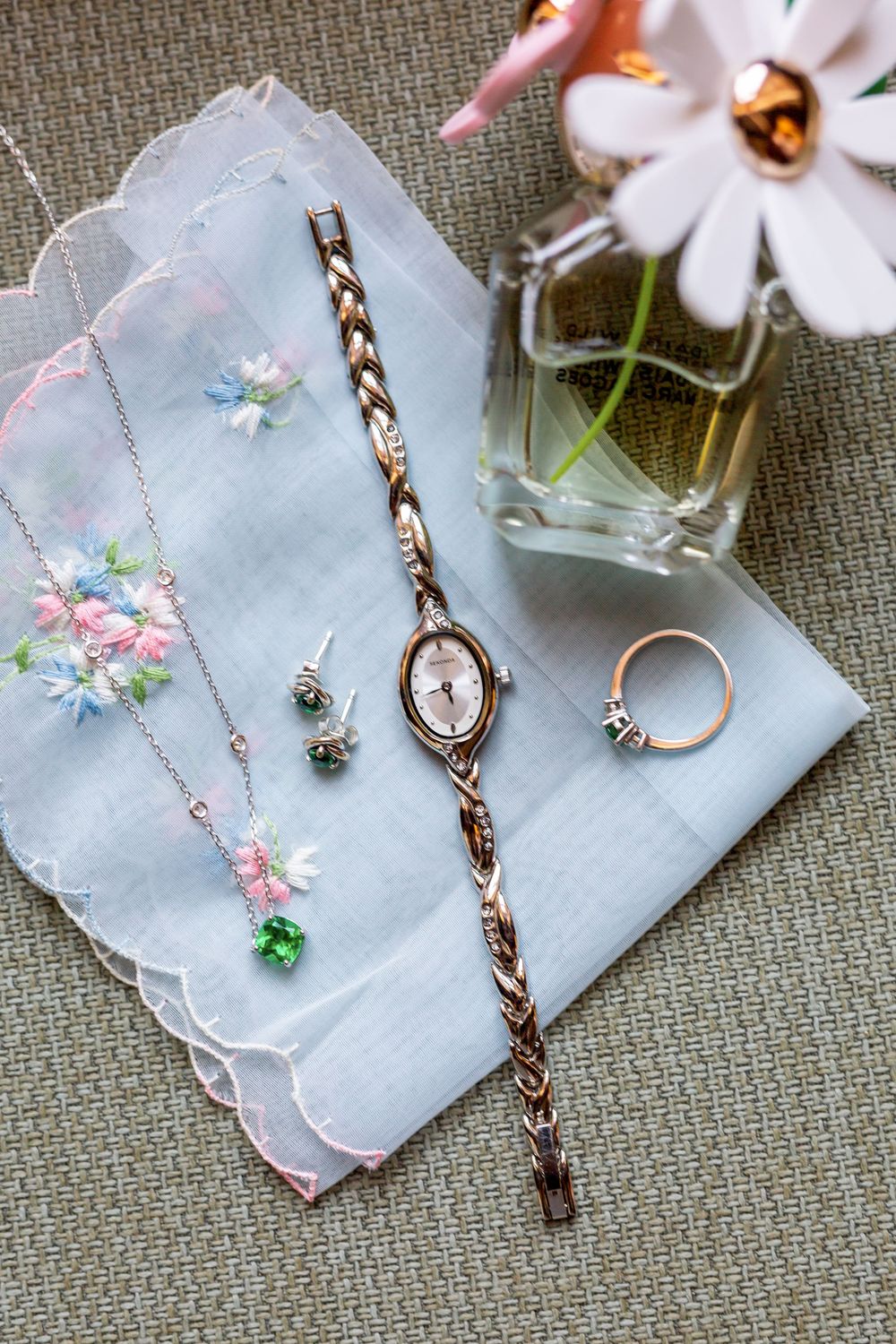 Delicate vintage-style jewelry pieces including necklaces and earrings displayed on pale blue fabric with floral embroidery details.