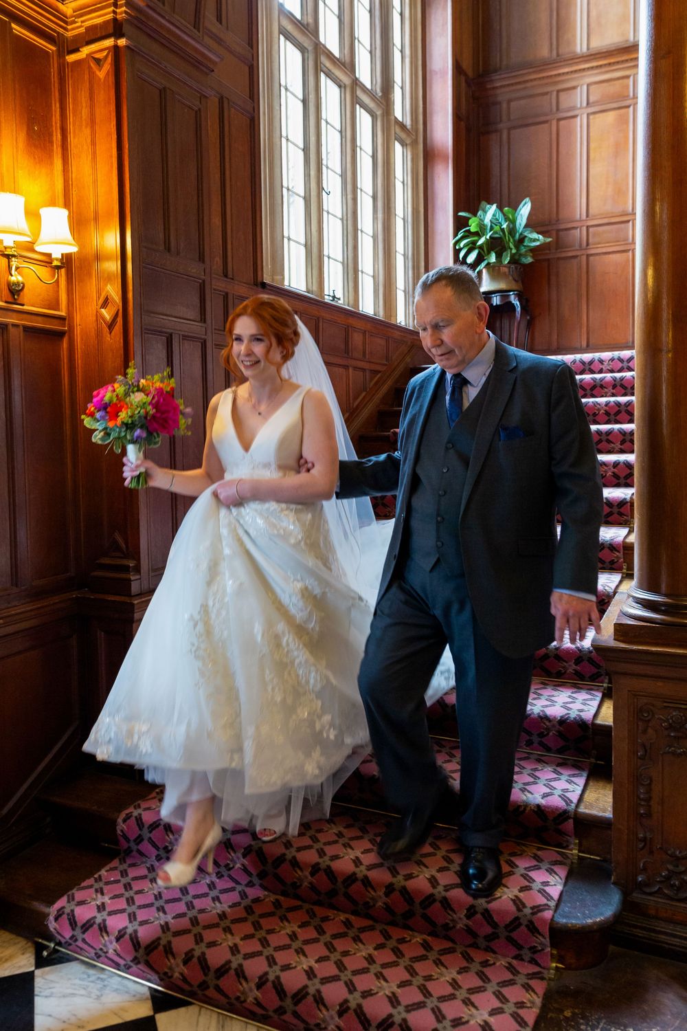 A couple dances together in an elegant wood-paneled room with patterned carpet and wall sconces.