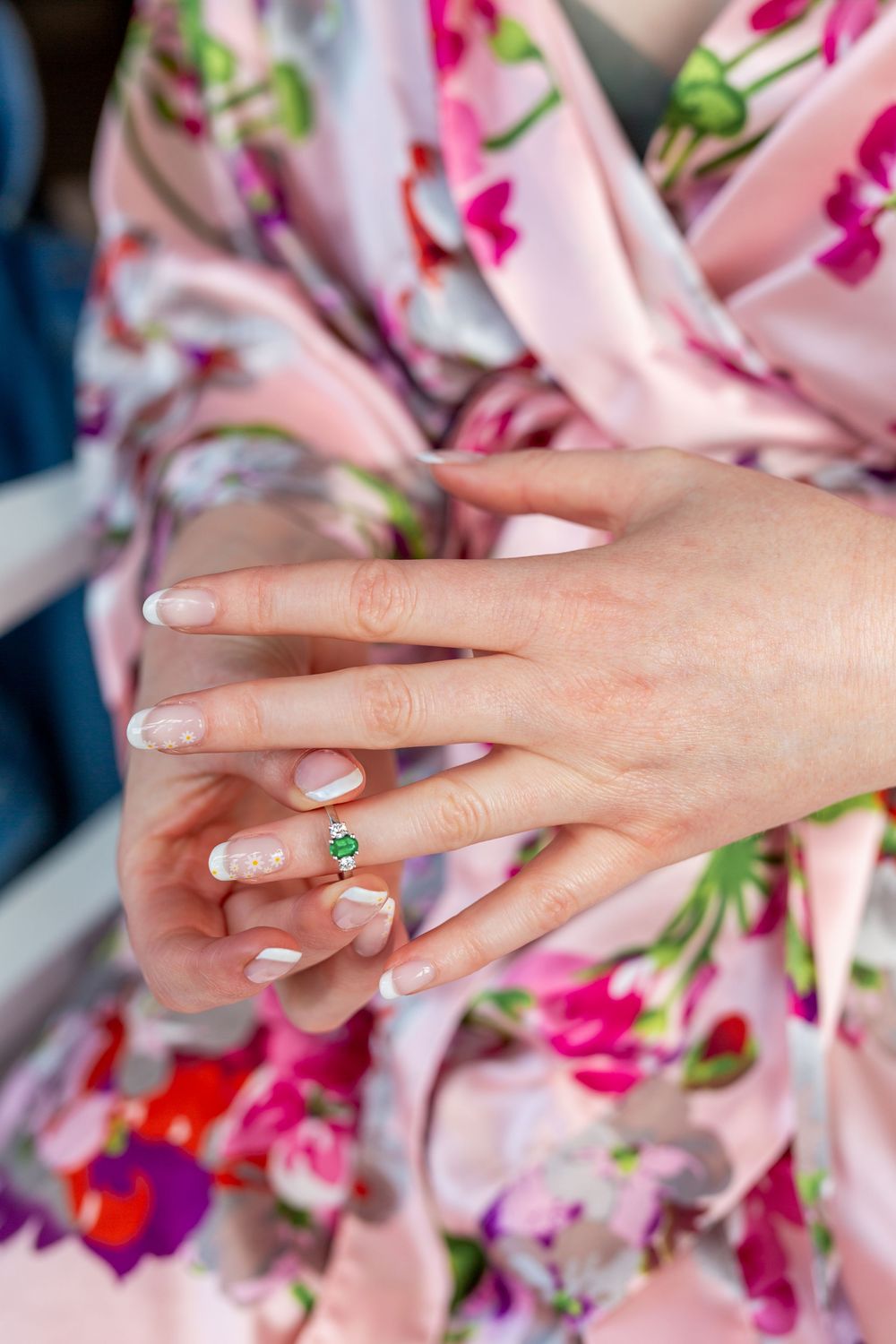 Close-up sequence showing hands displaying an emerald engagement ring against a floral pink background.