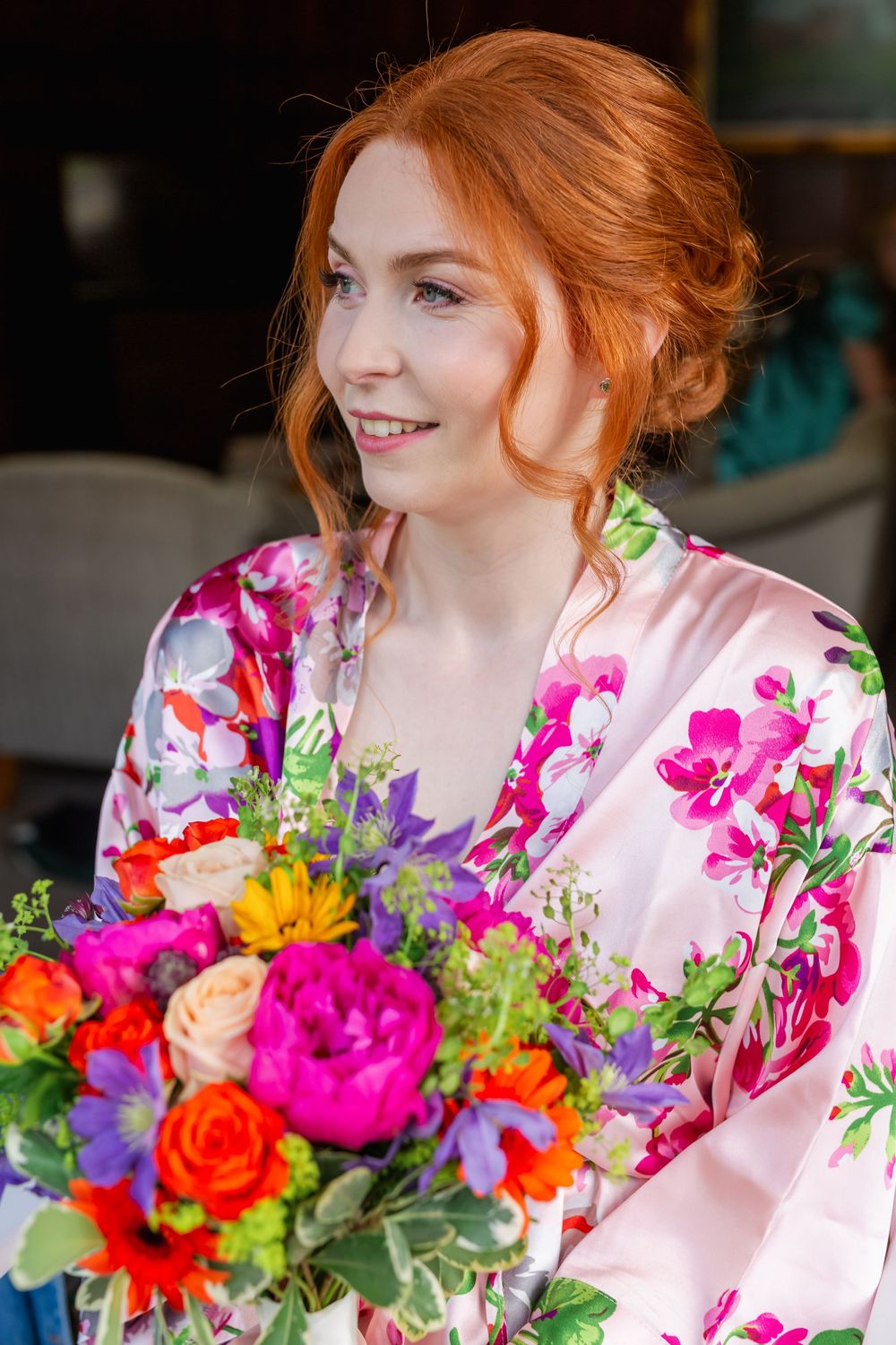 A person in a floral robe smiles while holding vibrant bouquets of pink, orange and purple flowers.