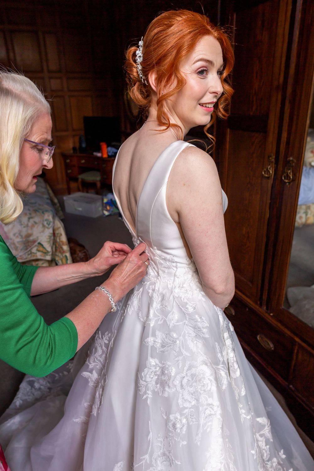 A series of photos showing someone helping to button up a white lace wedding dress with delicate floral details.