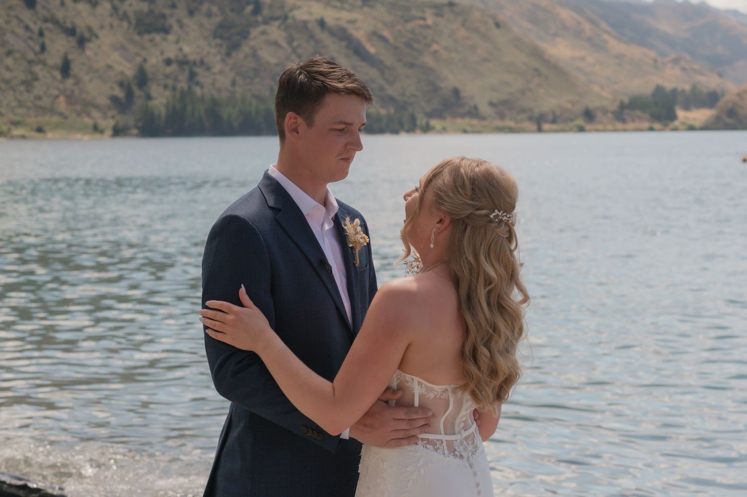 A couple shares a romantic moment by a stunning turquoise lake with snow-capped mountains in the background.