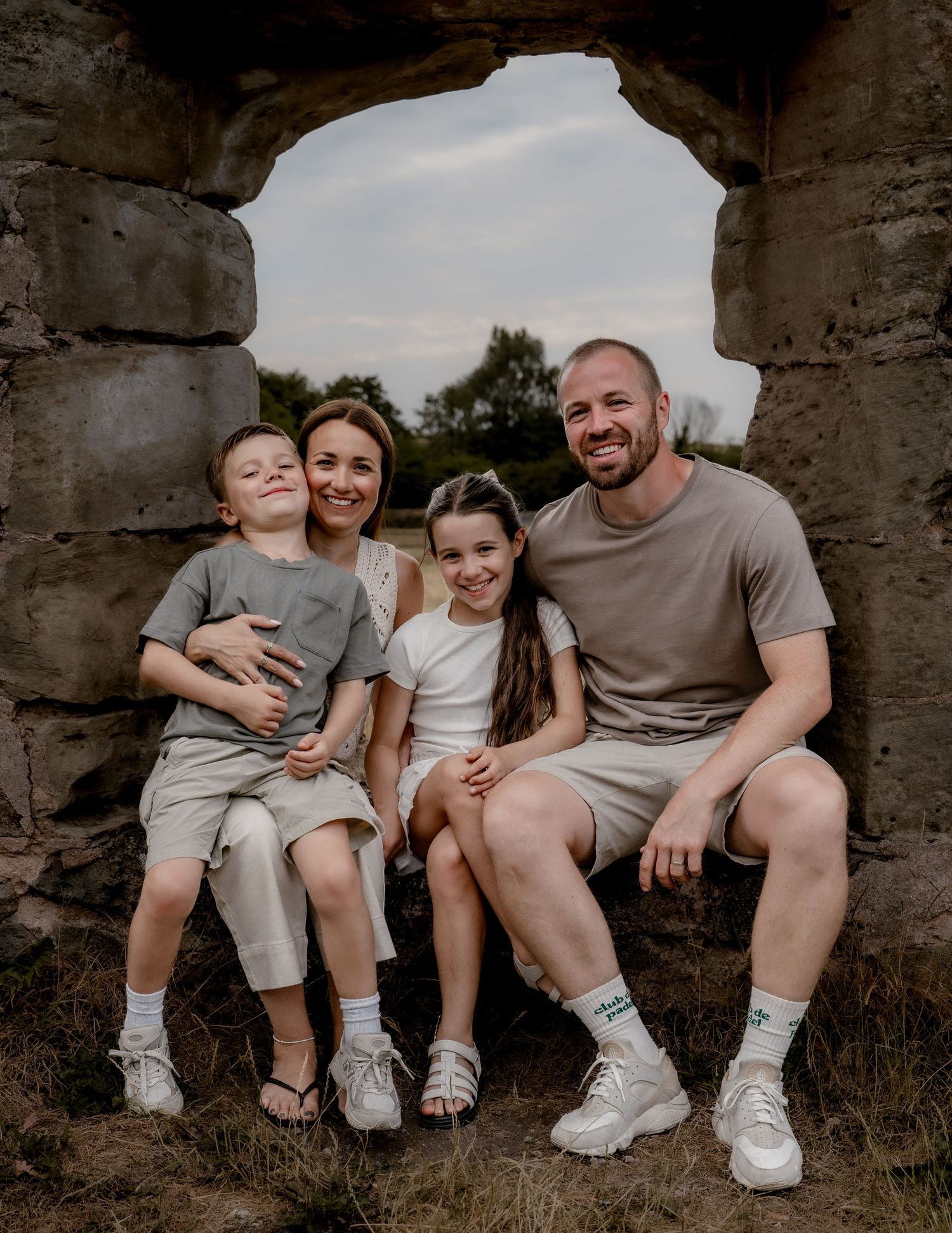 A family sits together on stone steps wearing coordinated casual outfits in white and gray for an outdoor photo session.