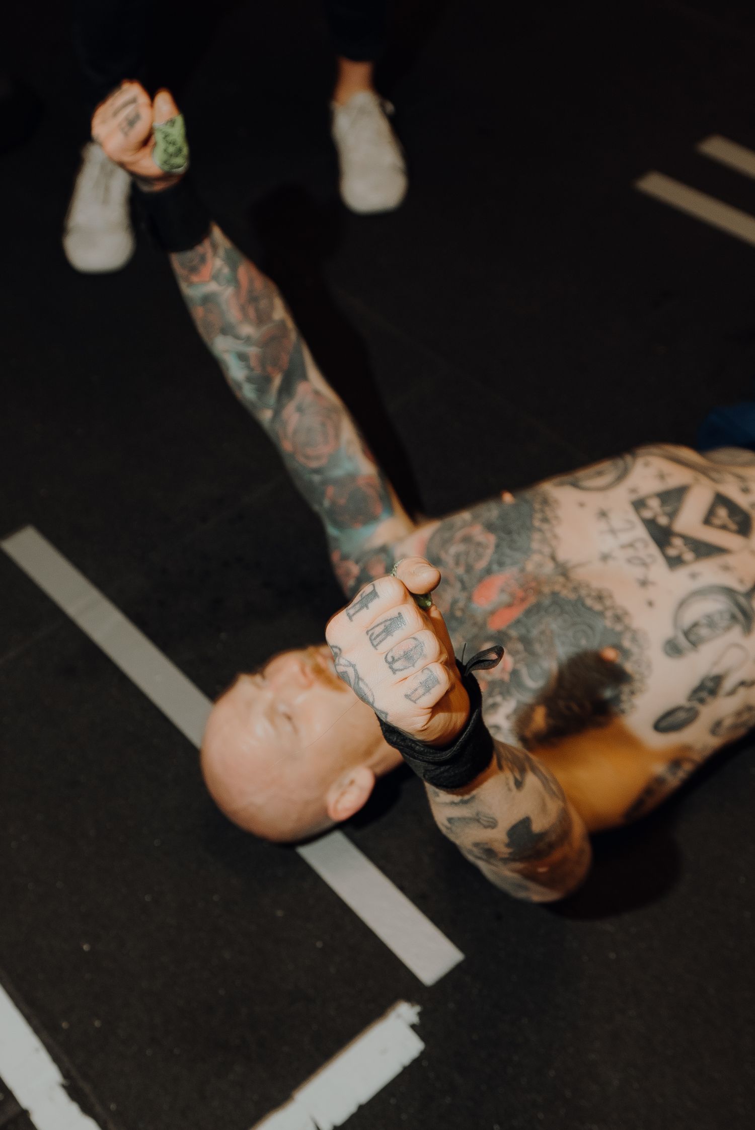 Heavily tattooed person lying on gym floor with exercise equipment.