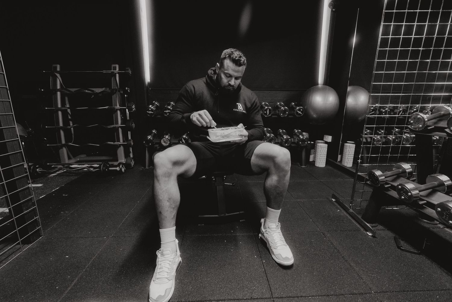 Athletic figure resting on gym equipment in a dark fitness environment.