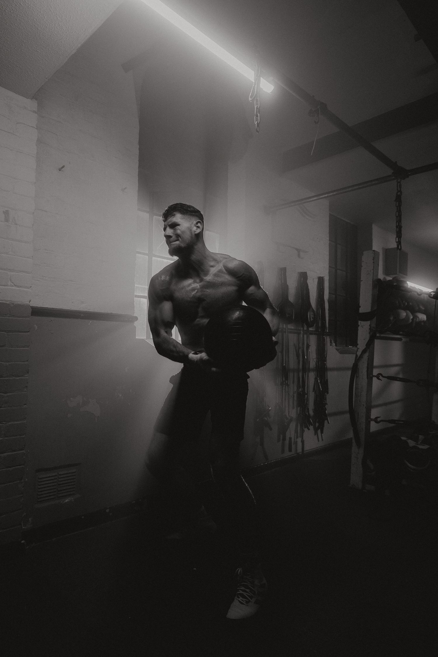A dramatic black and white photo of an athletic figure exercising in a dimly lit gym with moody lighting and shadows.