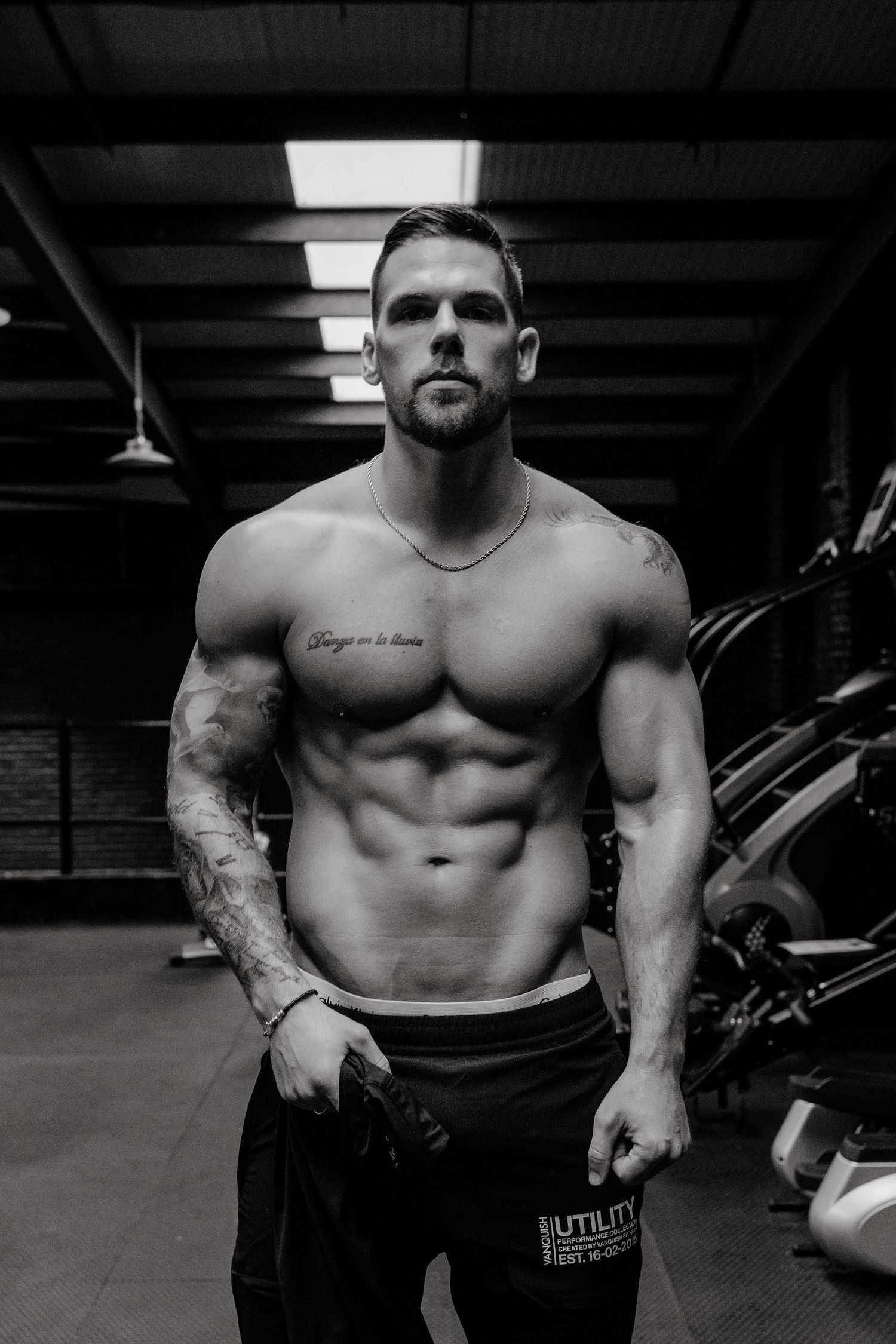 Black and white gym photo showing muscular physique with tattoos.