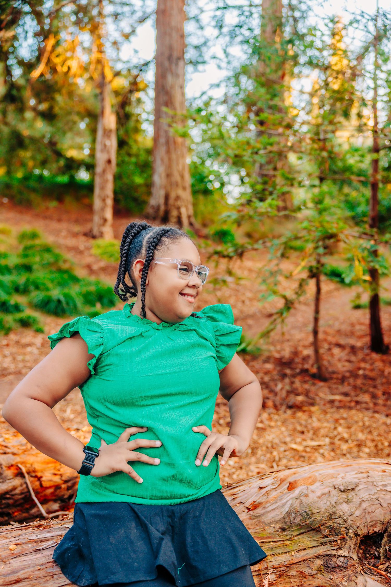 A joyful person in a bright green shirt and dark skirt poses playfully on fallen leaves in an autumn forest setting.